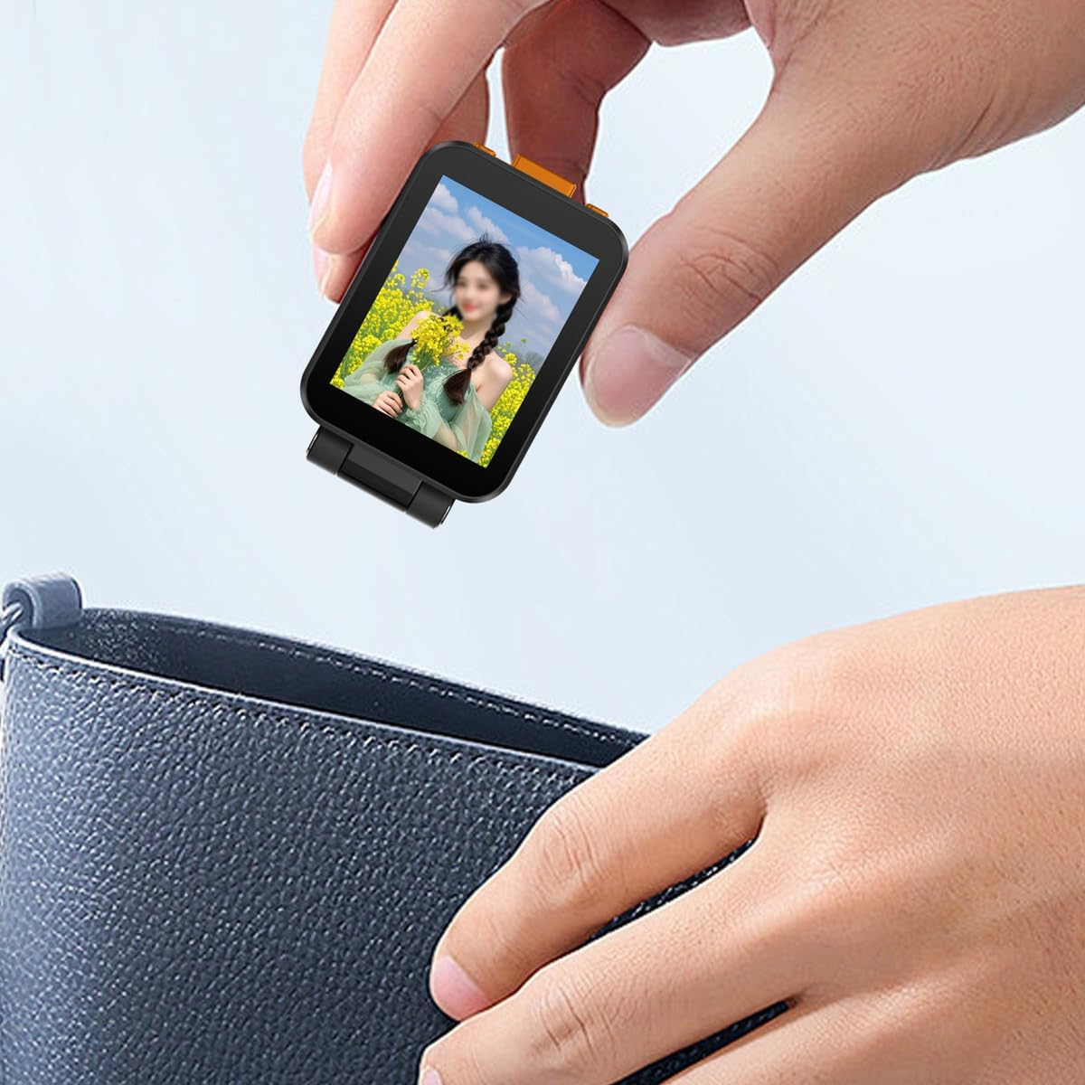 Eine Hand hält eine kleine schwarze Kamera mit Fotodisplay über eine offene blaue Tasche.