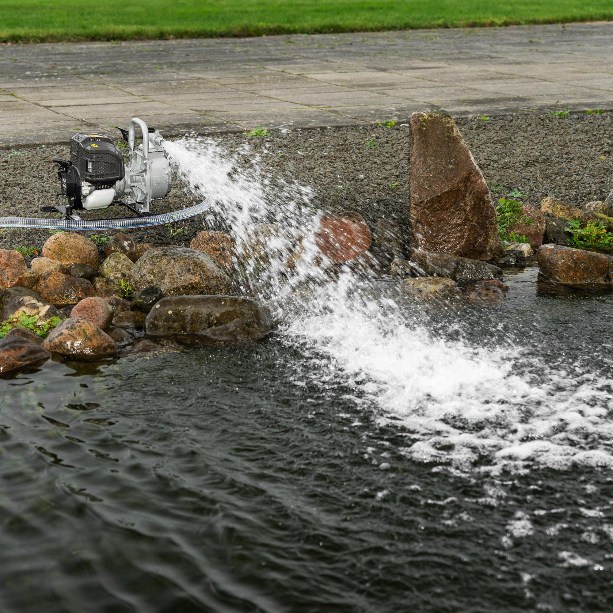 Eine Benzinwasserpumpe auf dem Boden pumpt Wasser in einen Teich mit Steinen.