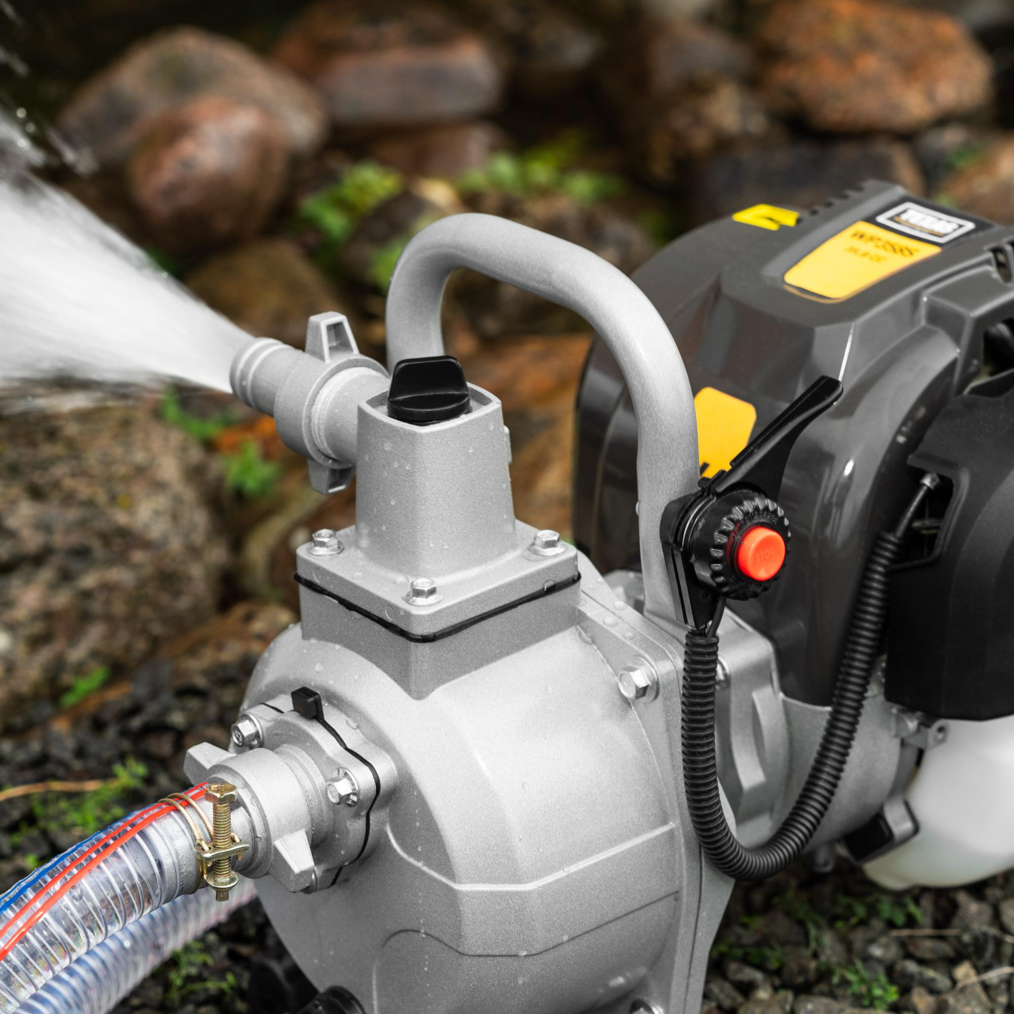 Eine graue Wasserpumpe mit angeschlossenen Schläuchen pumpt Wasser auf steinigem Untergrund.