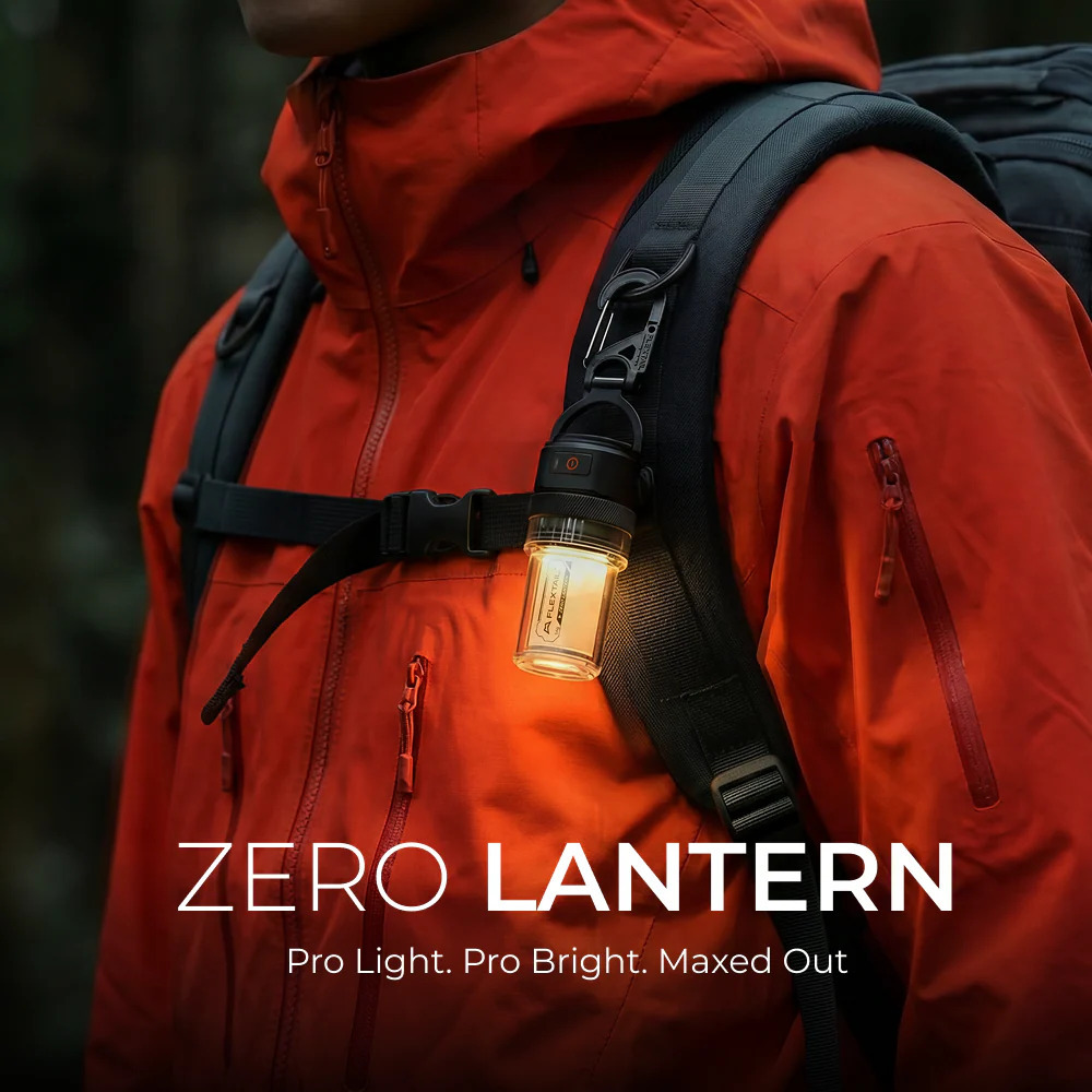 Eine kleine LED-Laterne hängt am Rucksackriemen einer Person in roter Jacke vor dunklem Waldhintergrund.