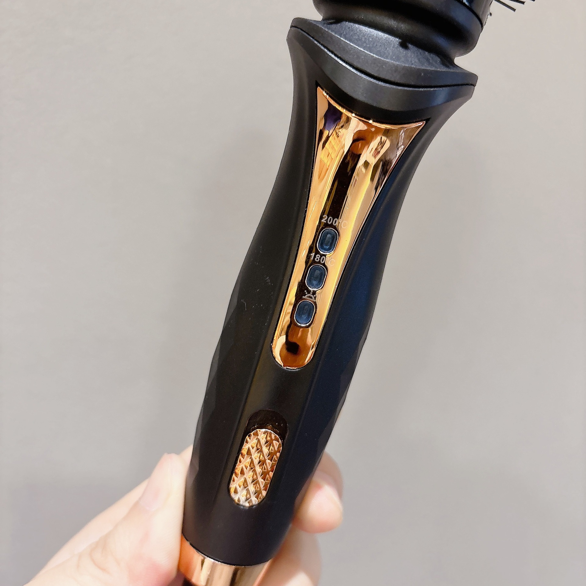 Eine Hand hält ein schwarzes und roségoldenes Haarstyling-Gerät mit Temperaturreglern vor schlichtem Hintergrund.