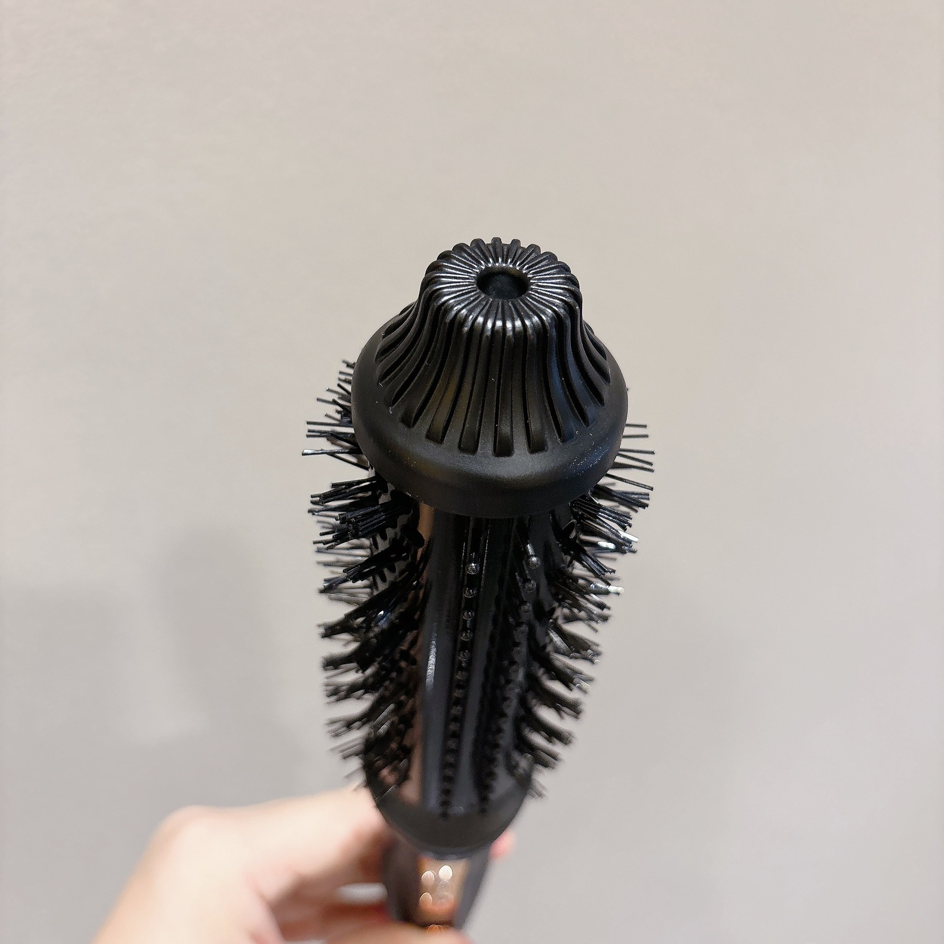 Nahaufnahme einer runden schwarzen Haarbürste mit Borsten, gehalten vor einem hellen Hintergrund.