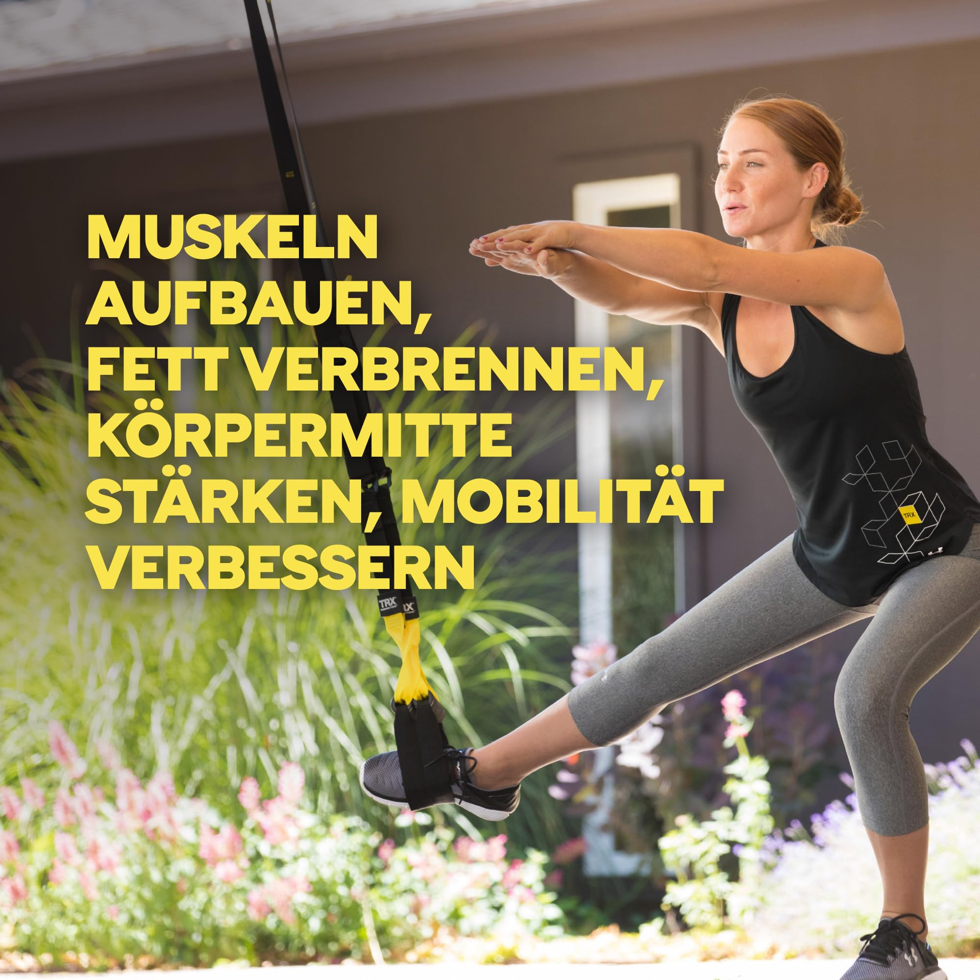 Eine Frau in Sportkleidung macht eine Kniebeuge mit Schlingentrainer vor Grünanlagen.
