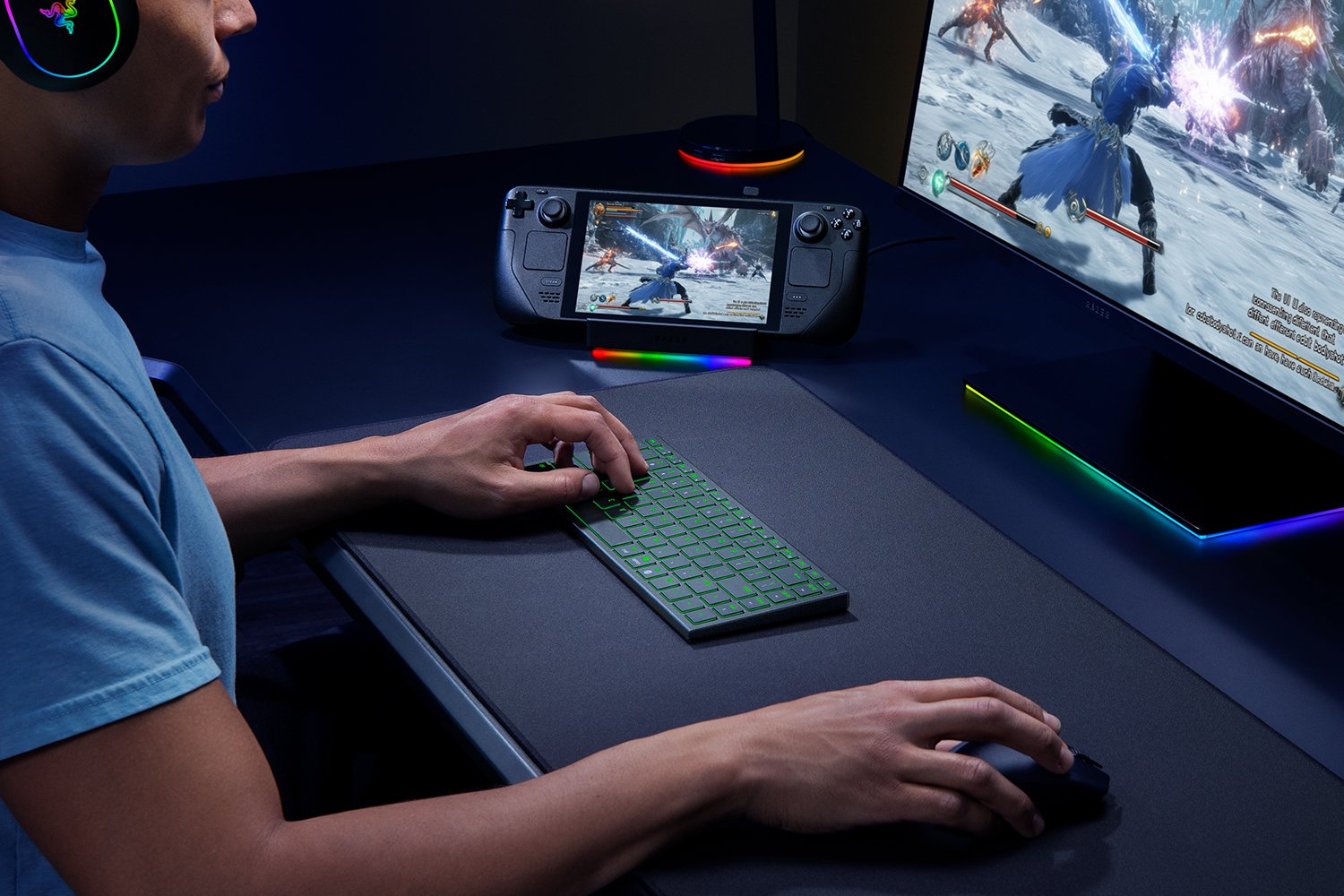 Un giocatore usa una tastiera e un mouse compatti su una scrivania con più schermi e illuminazione RGB.