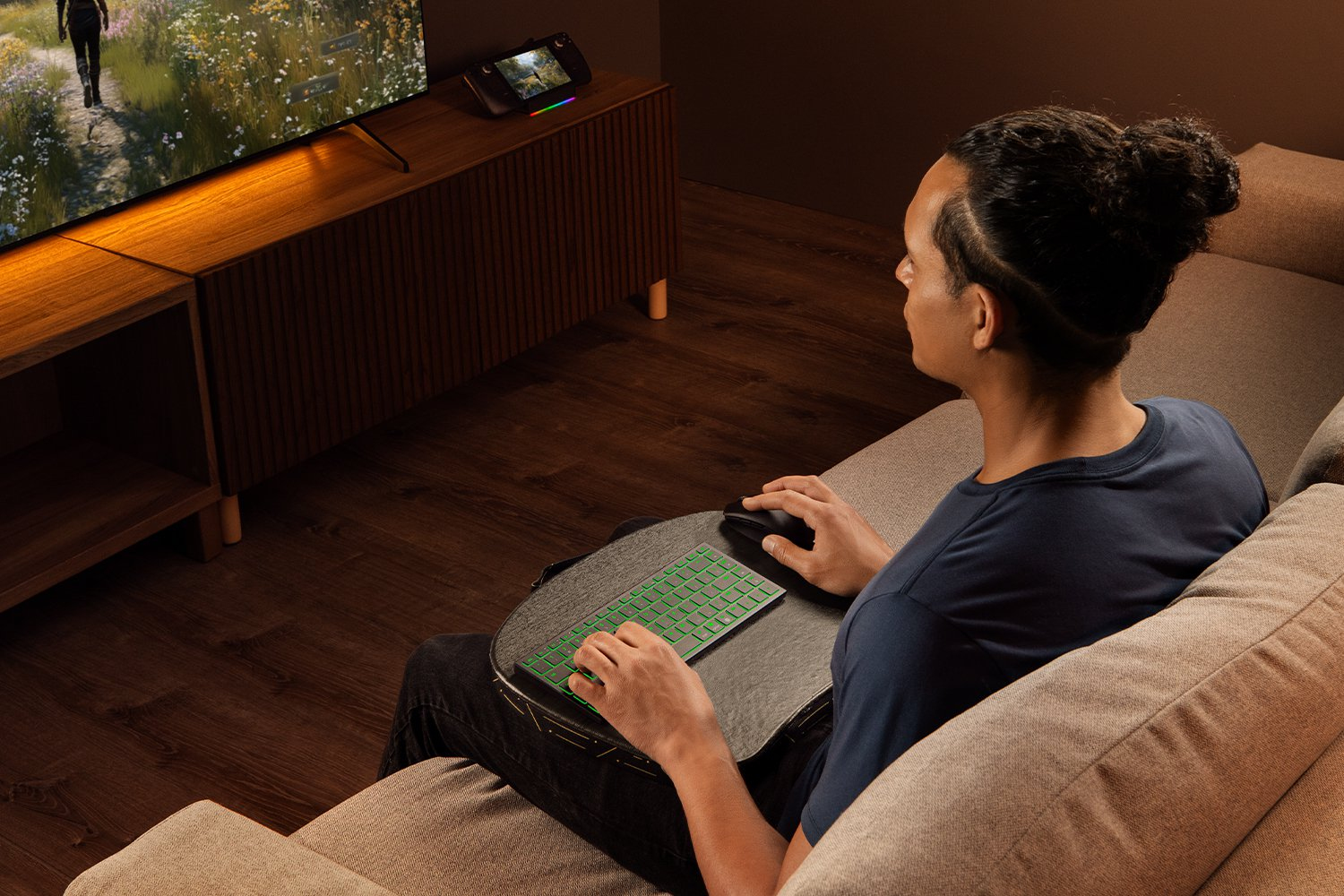 Un uomo sul divano usa tastiera e mouse per giocare su una TV.