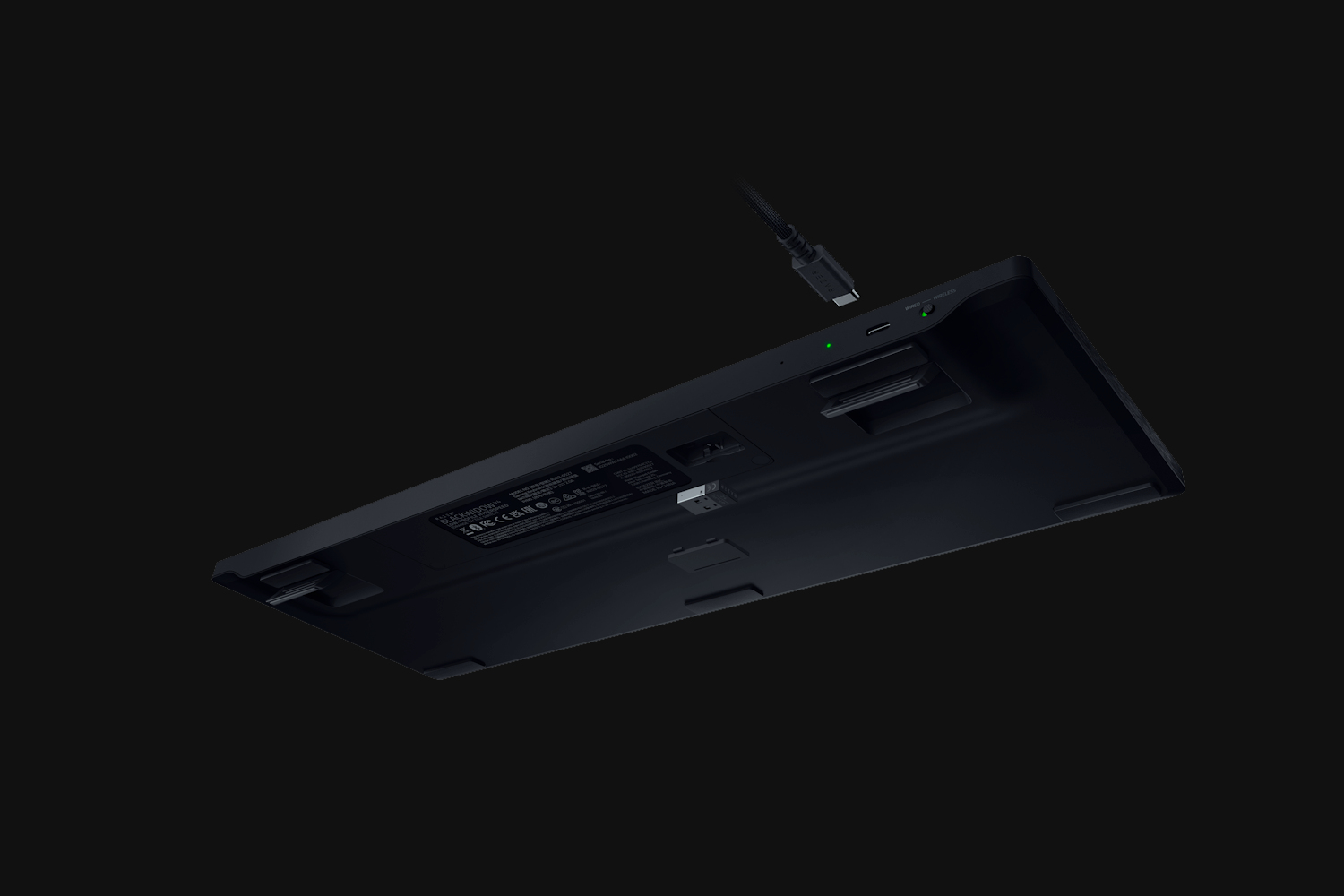 La parte inferiore di una tastiera nera con un cavo USB-C collegato su sfondo scuro.