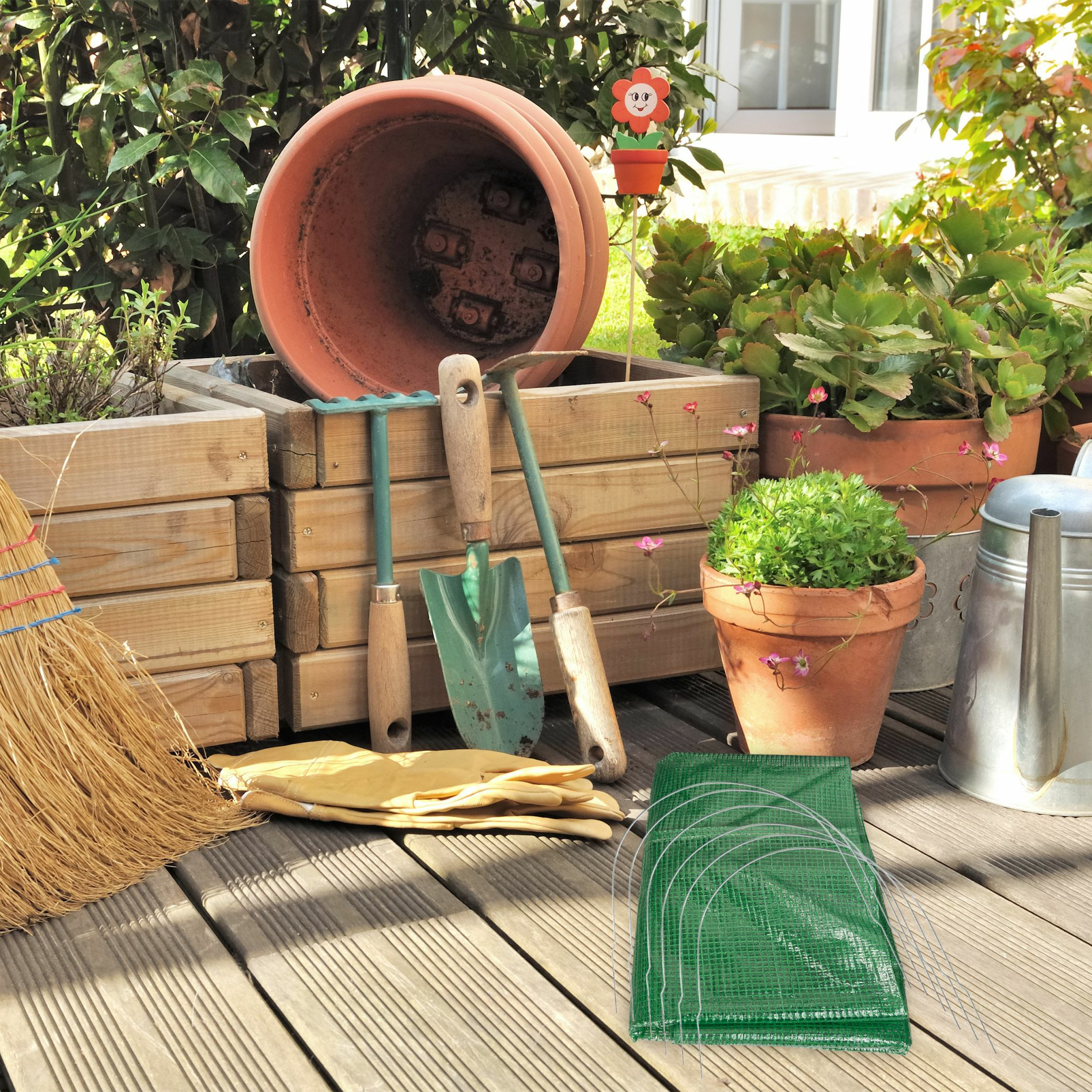 Gartengeräte, Blumenkübel und Handschuhe auf Holzterrasse.