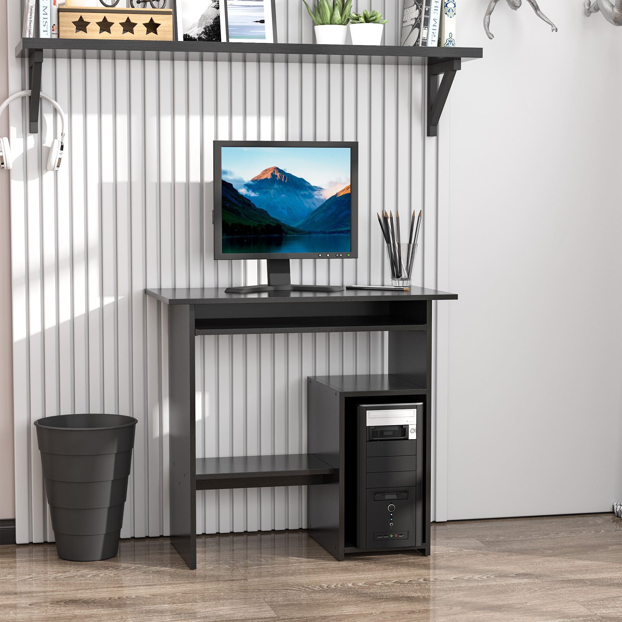 Una scrivania nera con monitor, torre PC e un cestino dei rifiuti accanto.