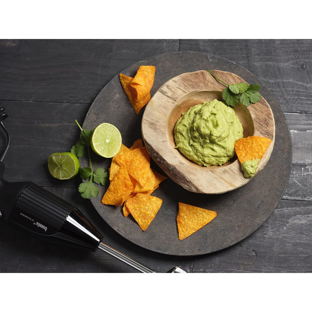 Una ciotola di legno con guacamole, nachos, lime e un frullatore.
