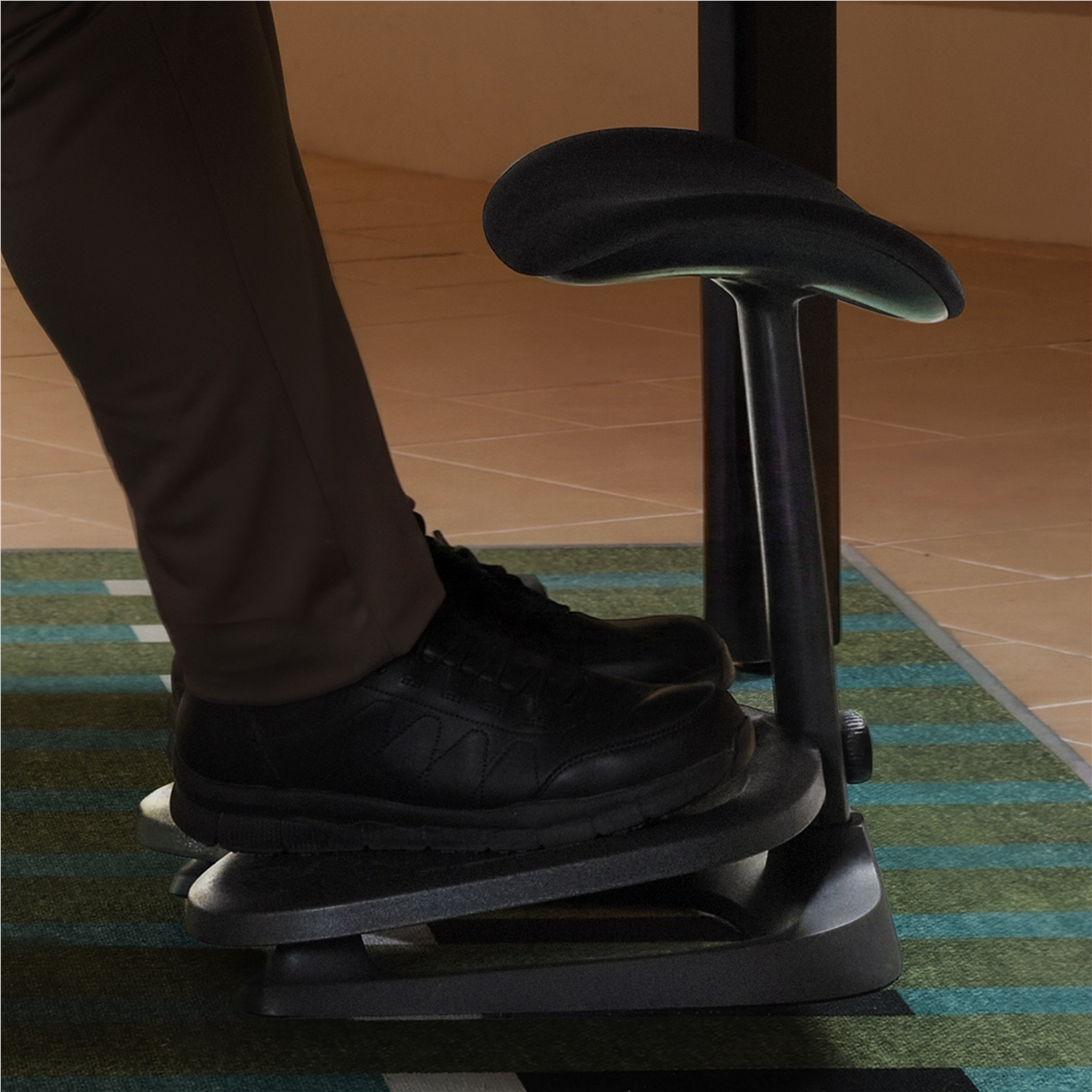 Persona apoyada en un taburete ergonómico negro con los pies en una tabla.