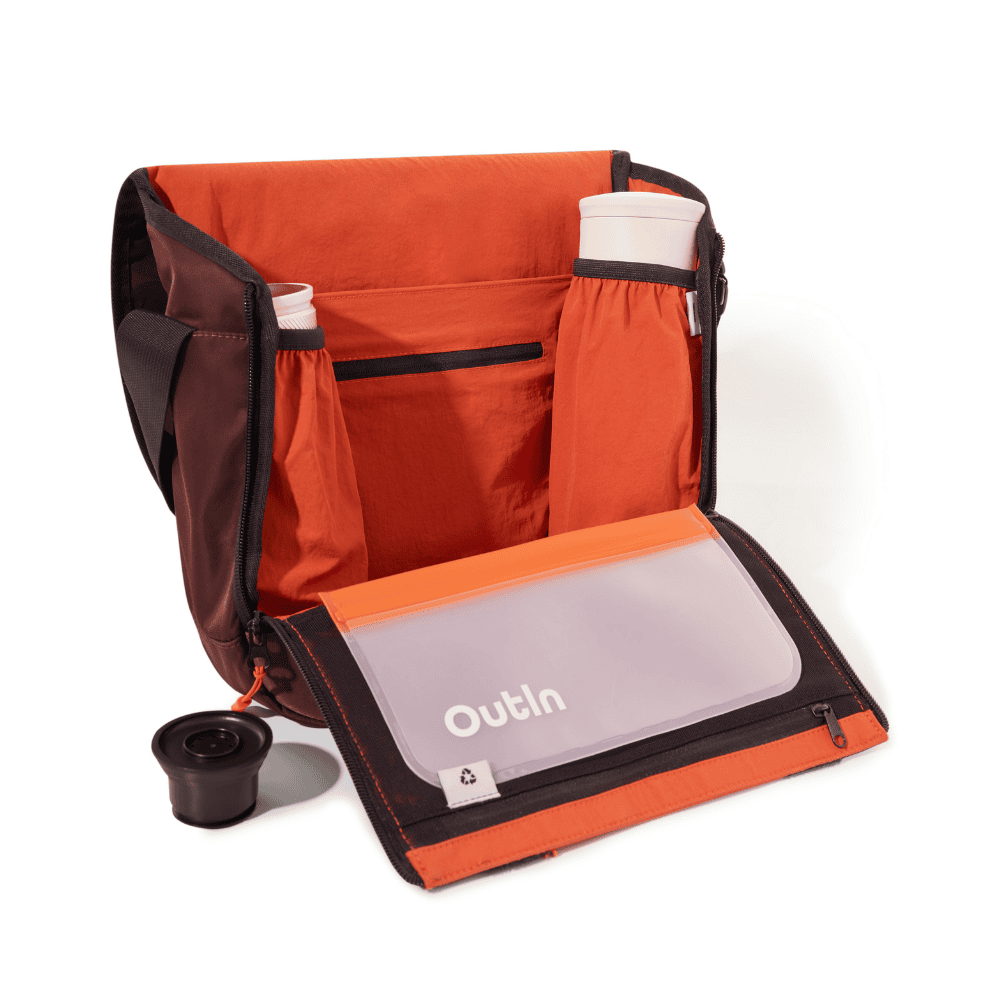 Bolsa abierta marrón y naranja con dos botellas de agua dentro y una taza negra separada enfrente.