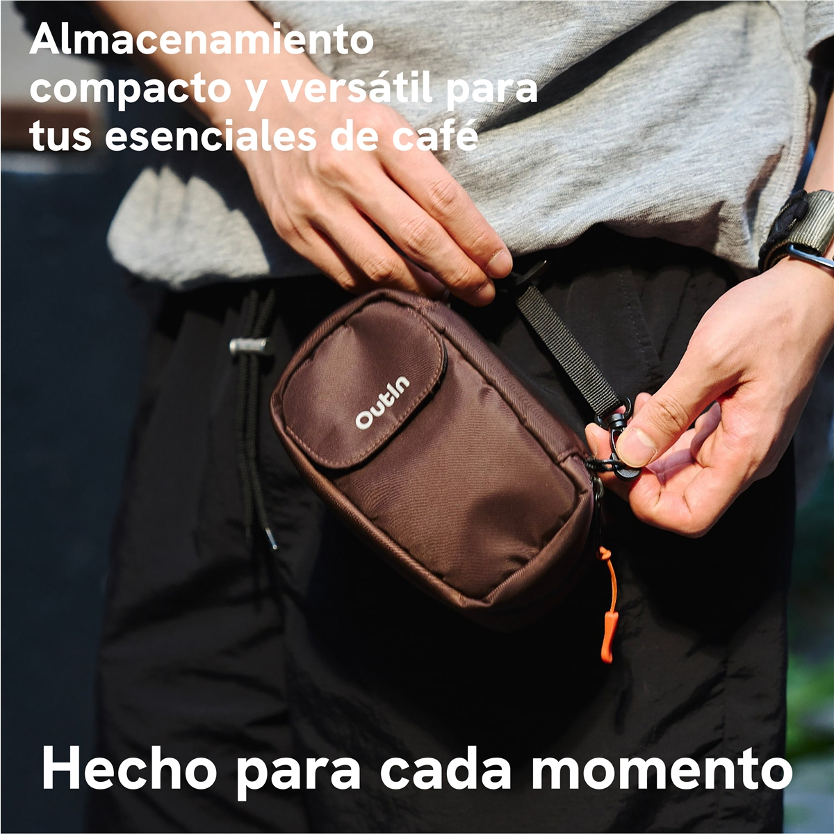 Una persona con camisa gris y pantalones cortos negros sostiene una pequeña bolsa marrón Outin.