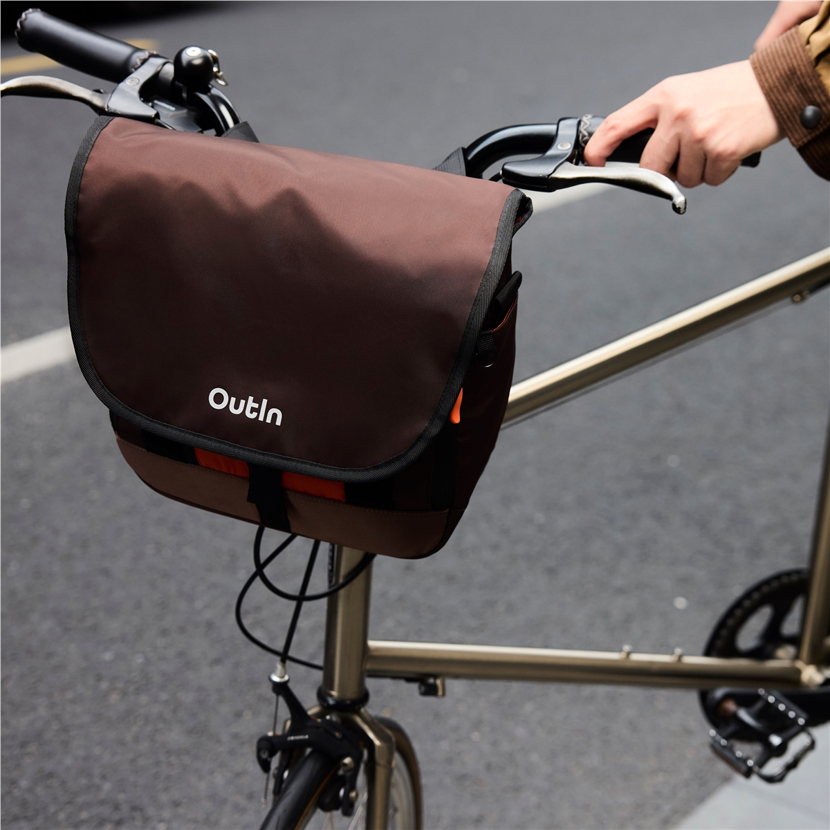 Una bolsa marrón para manillar de bicicleta Outin montada en el cuadro sobre asfalto.