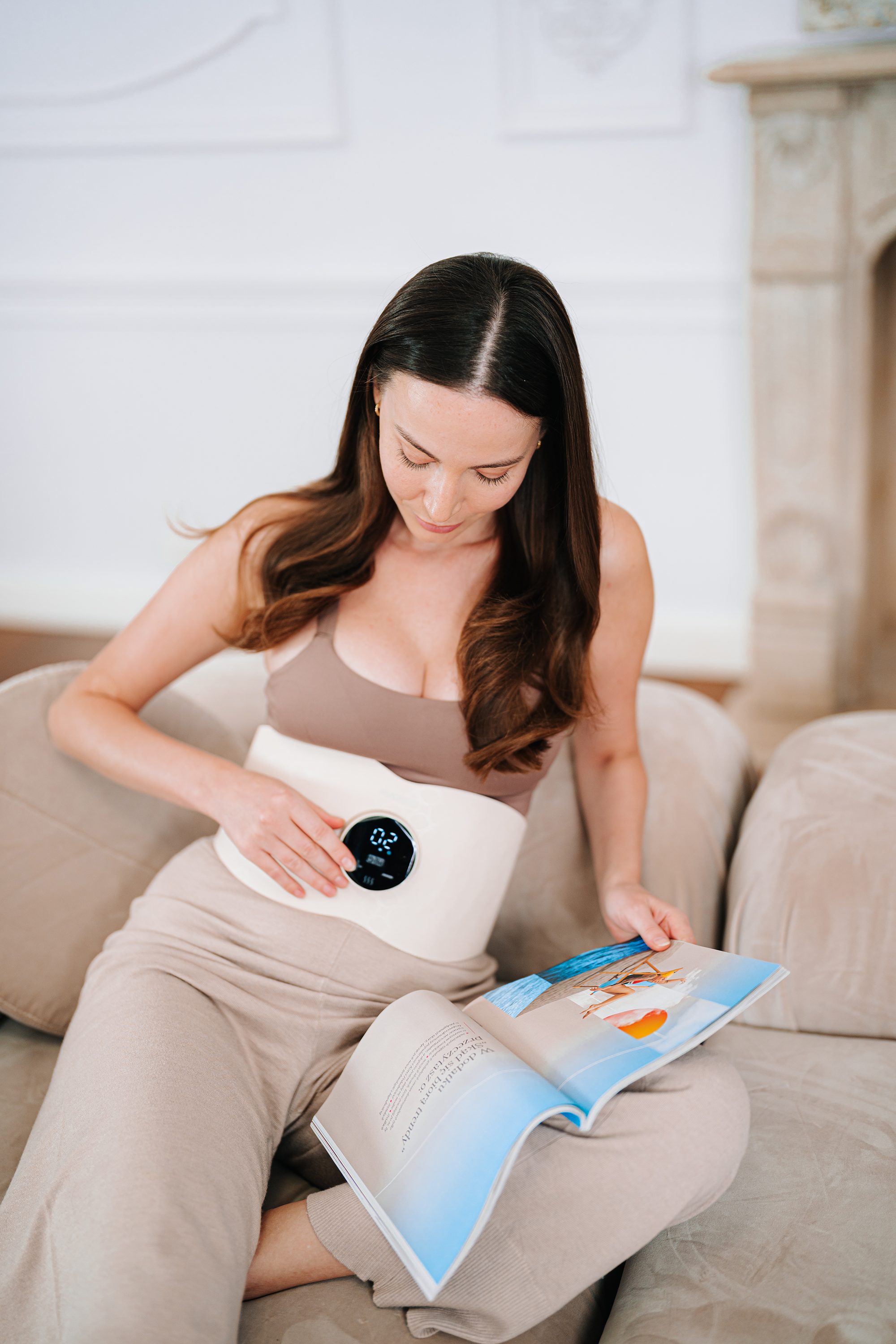 Frau sitzt auf dem Sofa, trägt einen Bauchgürtel mit Display und liest ein Magazin.