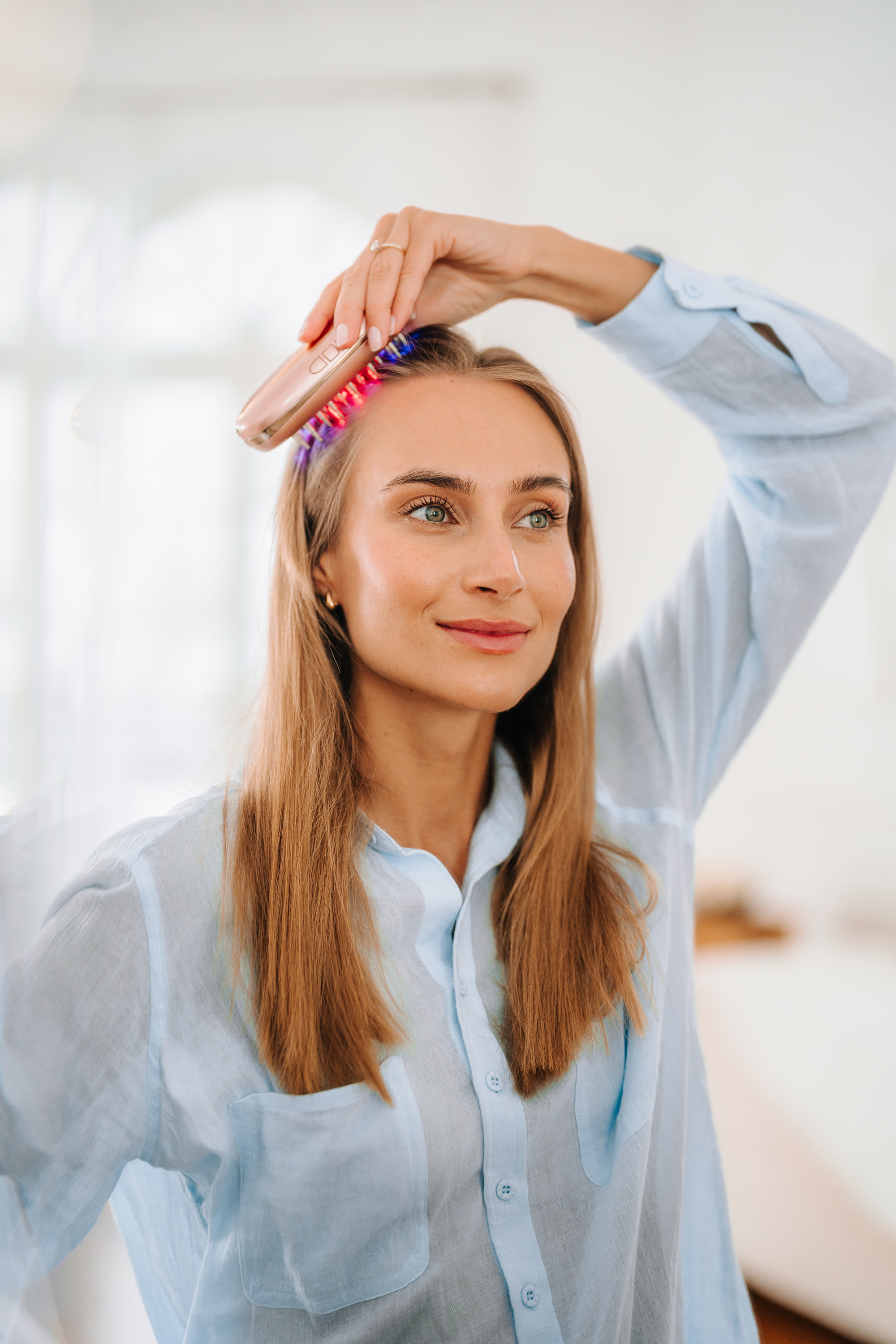 Una mujer con camisa azul usa un dispositivo de luz roja para el crecimiento del cabello.