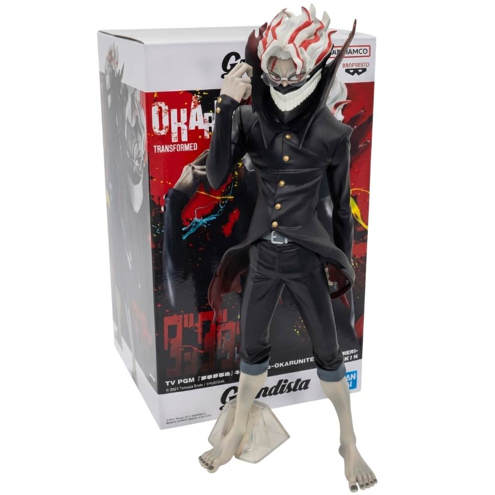 Una figure anime di Okarun in abito nero con capelli bianchi e rossi davanti alla scatola.