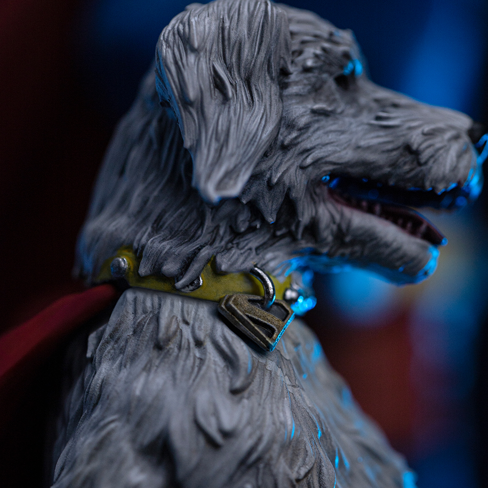 Primo piano di una statuetta di cane grigio con collare giallo e mantello rosso su sfondo blu e rosso.