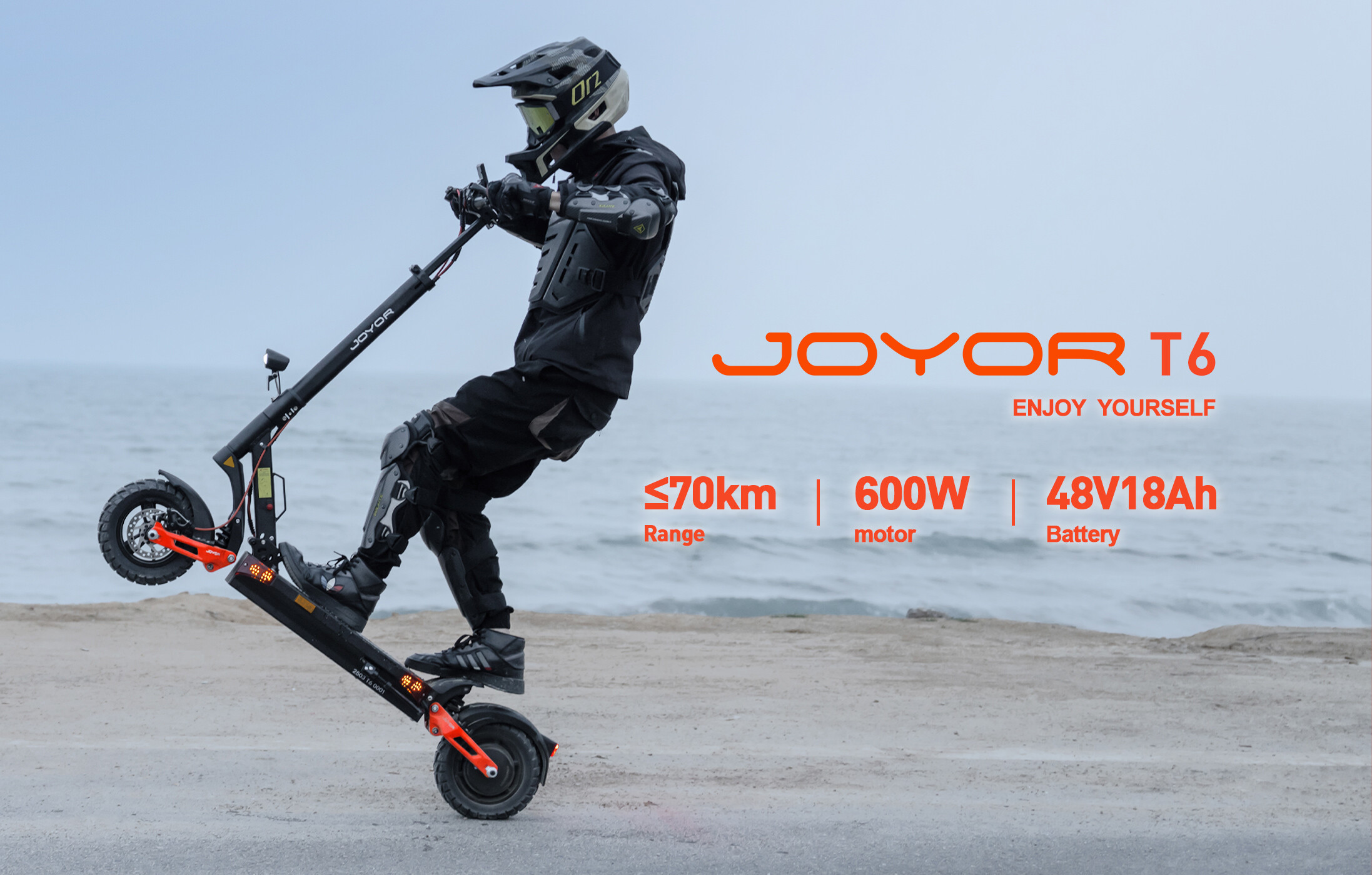 Un pilota con casco e armatura fa un'imennata su un monopattino elettrico Joyor T6 vicino al mare.