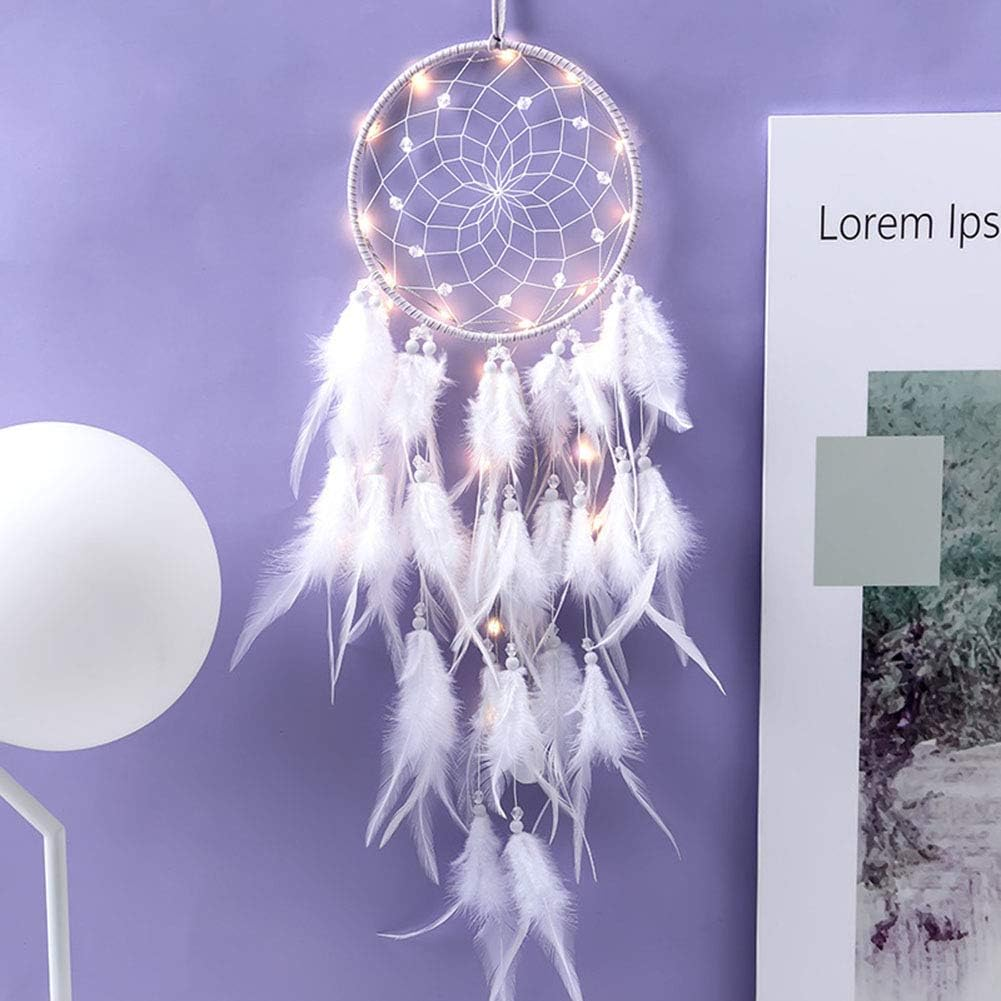 Ein weißer Traumfänger mit Lichterkette und Federn hängt an einer lila Wand neben einem Bild.
