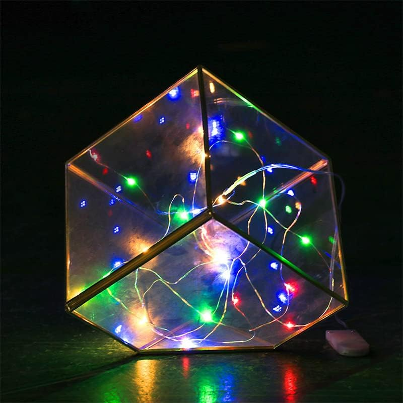 Eine polygonale Glaslampe mit Metallrahmen, gefüllt mit bunten Lichterketten vor dunklem Hintergrund.