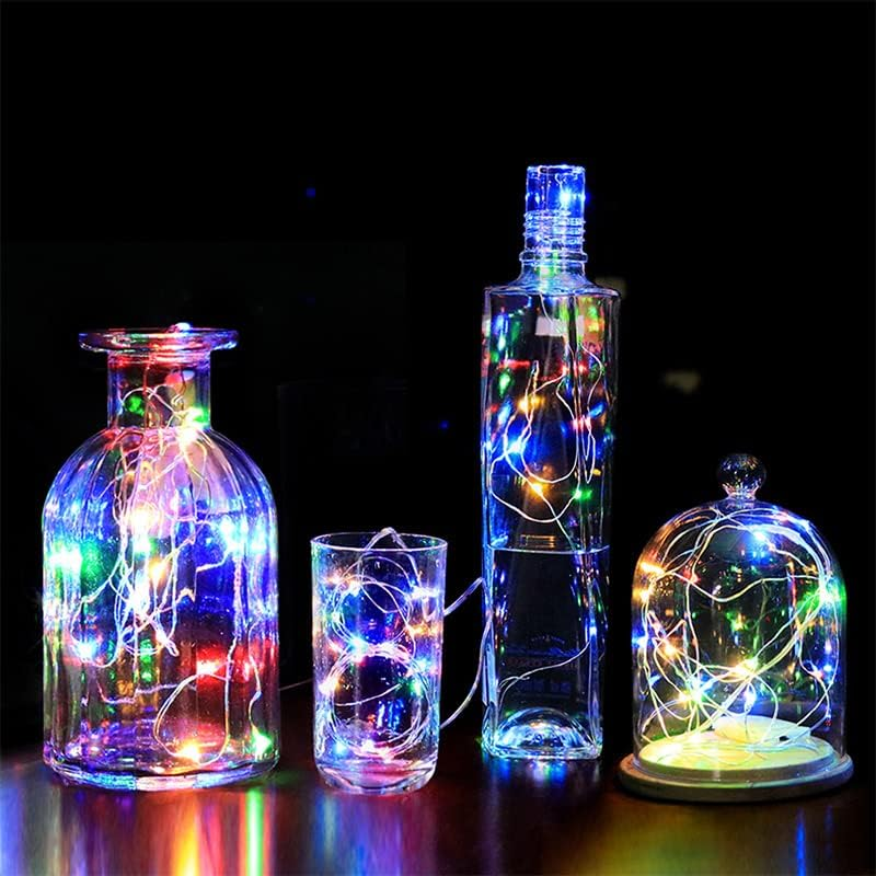 Vier Glasgefäße und eine Tasse, gefüllt mit bunten Lichterketten, stehen auf einem dunklen Tisch.