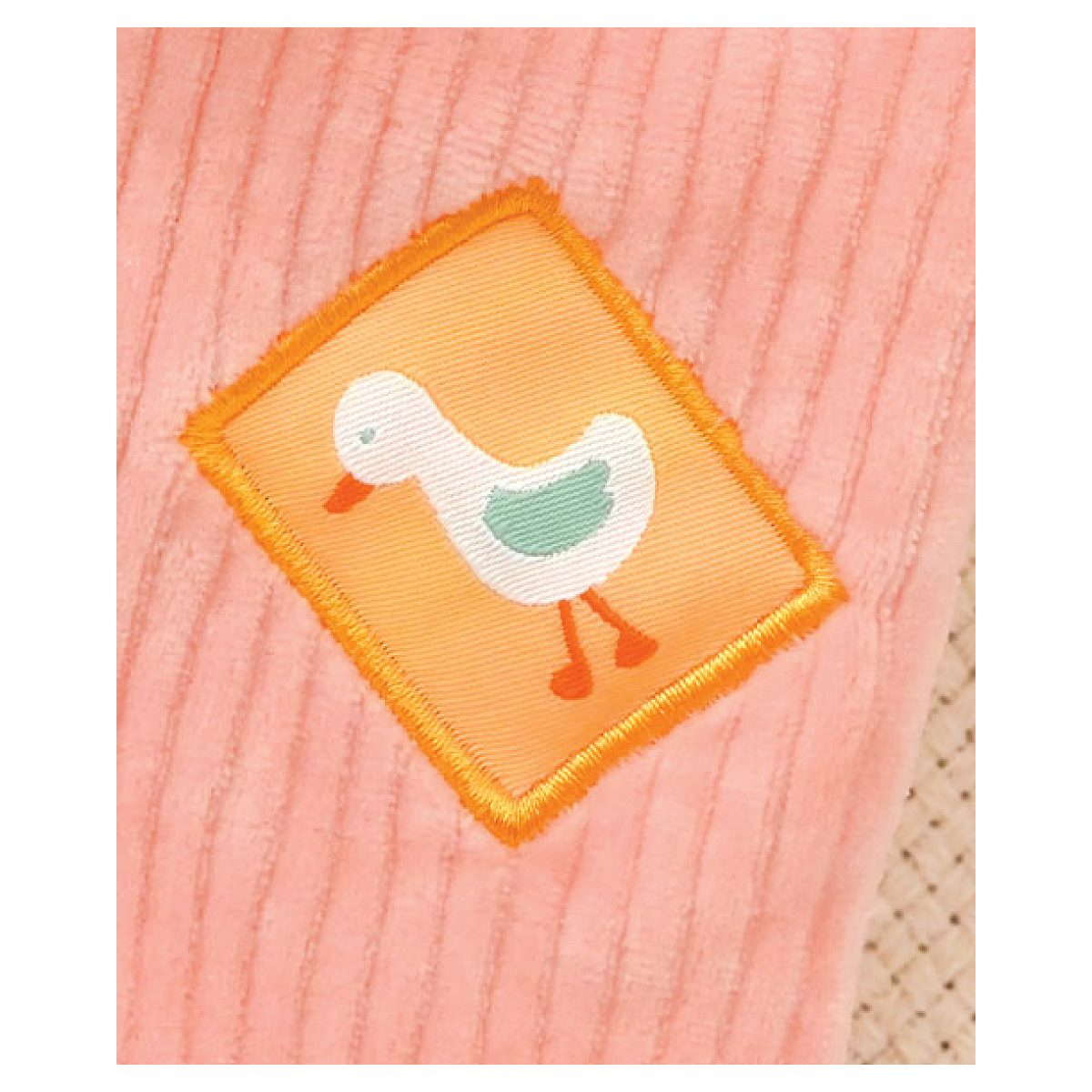 Ein aufgestickter weißer Vogel mit orangem Schnabel und grünen Flügeln auf einem orangefarbenen Patch auf rosa Stoff.