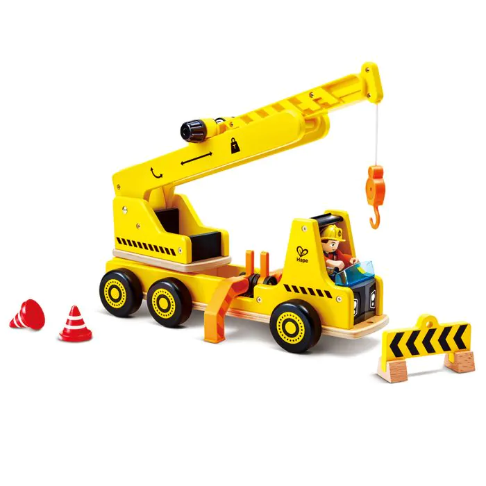 Ein gelber Spielzeug-Kranwagen aus Holz mit Fahrer, zwei kleinen roten Pylonen und einer gelb-schwarzen Absperrung.