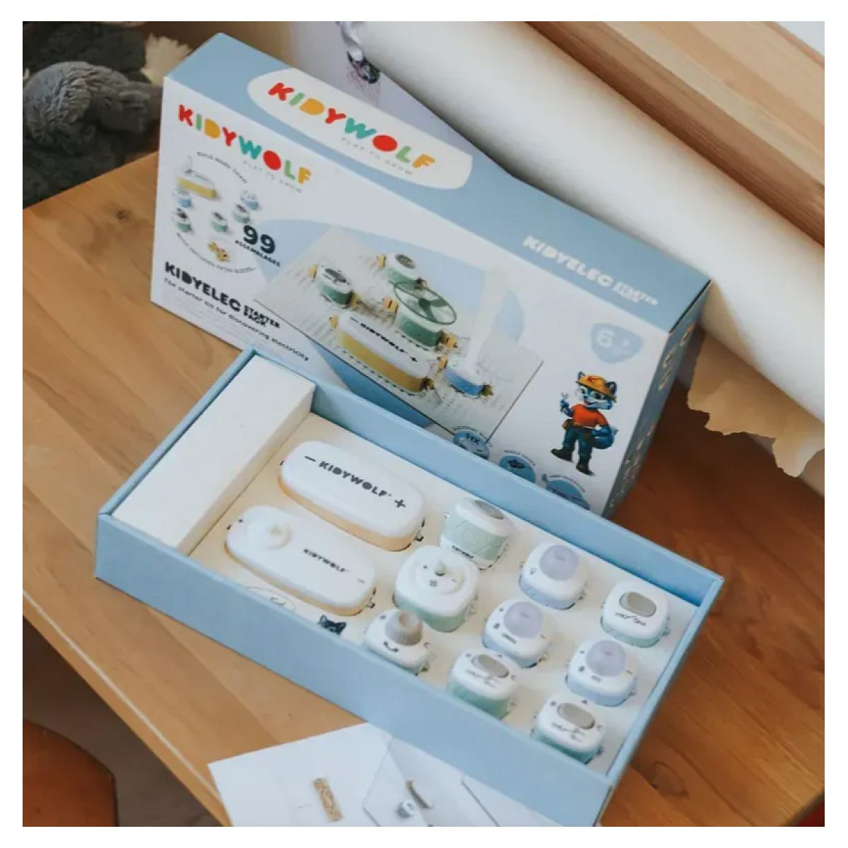 Ein offener Kiddywolf Starter-Kit-Karton mit verschiedenen elektrischen Bauteilen liegt auf einem Holztisch.