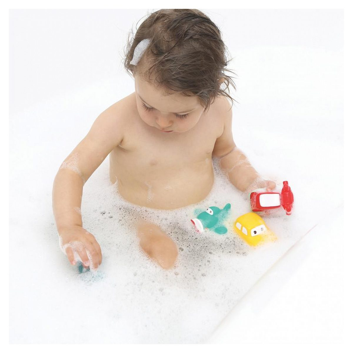 Ein Kleinkind spielt in einer weißen Badewanne voller Seifenwasser und bunten Spielzeugfahrzeugen.