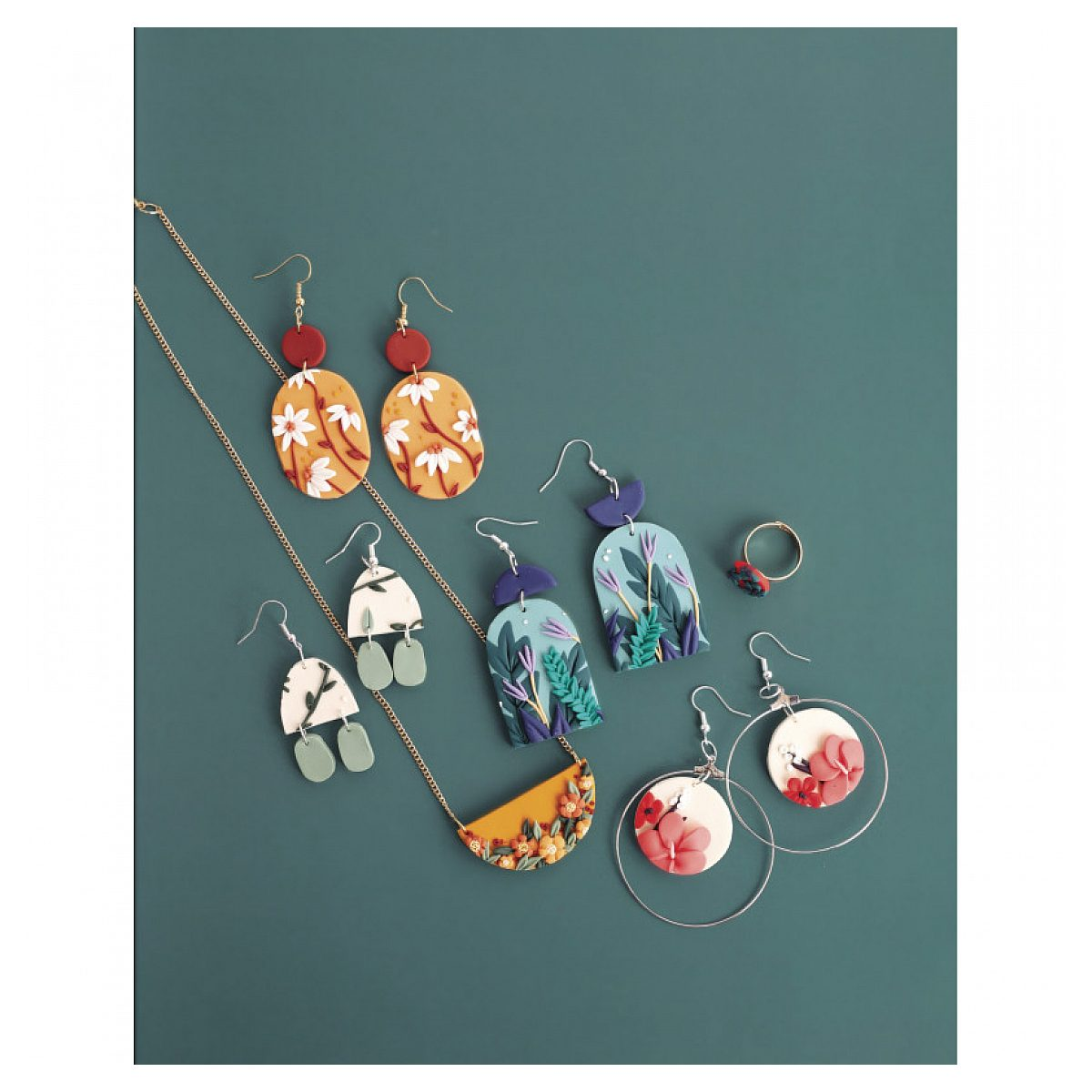 Handgemachter Schmuck aus Fimo mit Ohrringen, Halskette und Ring auf türkisem Hintergrund.