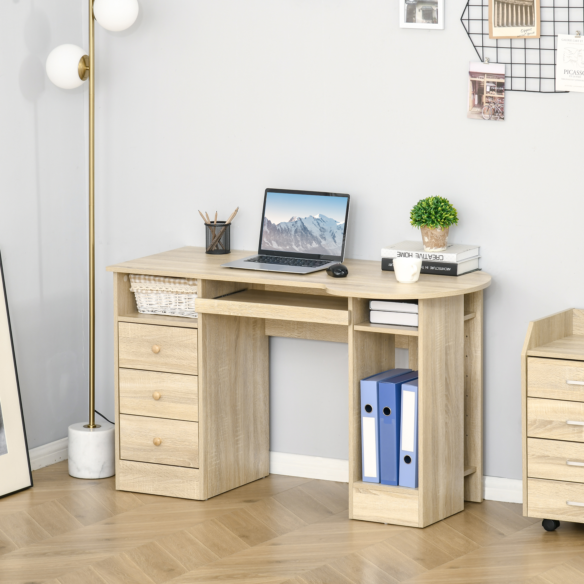 Una scrivania in legno chiaro con laptop, raccoglitori, lampada e decorazioni in una stanza con pavimento in legno.