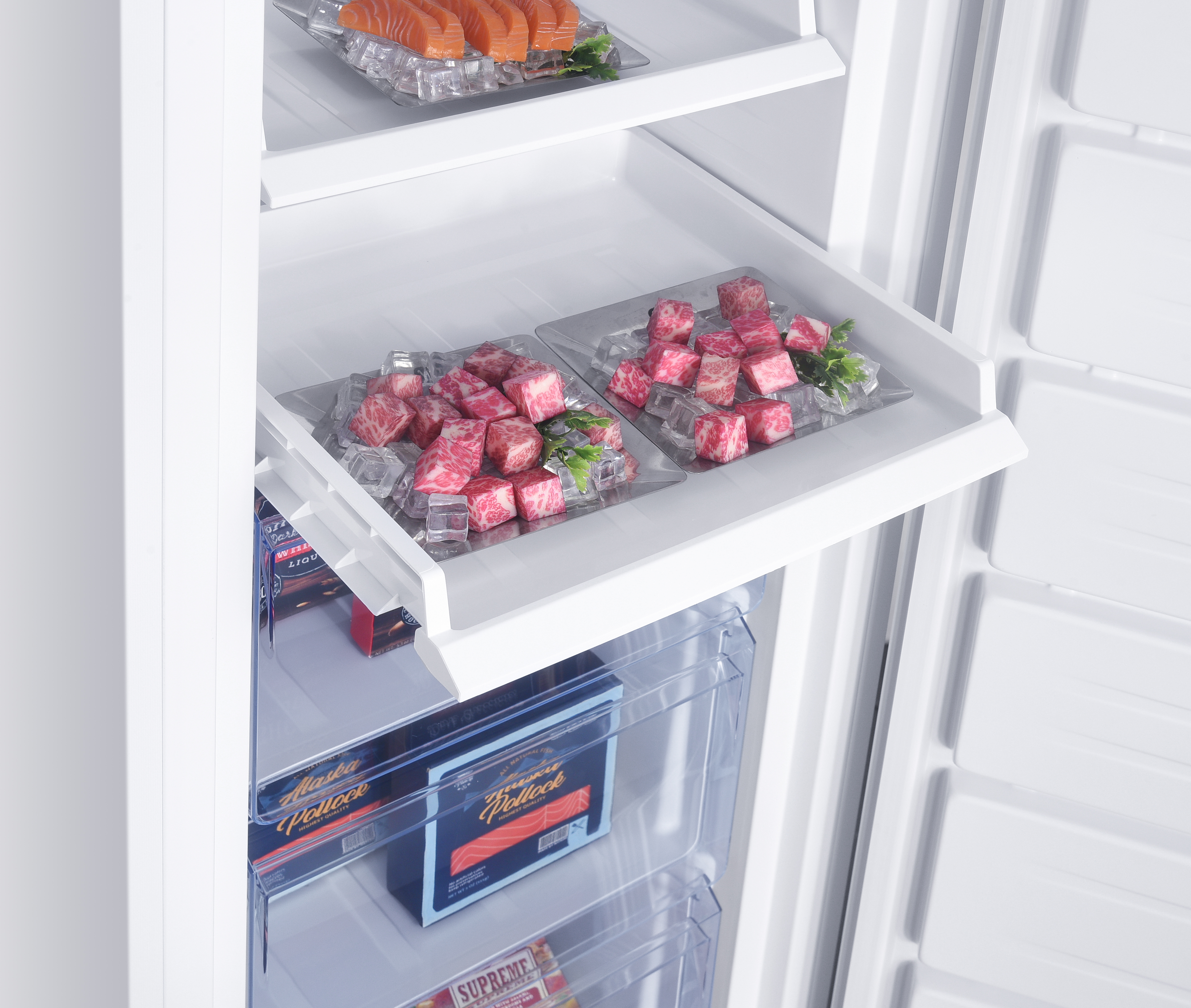 Un réfrigérateur blanc ouvert contenant des plateaux de viande et de poisson en cubes sur de la glace.