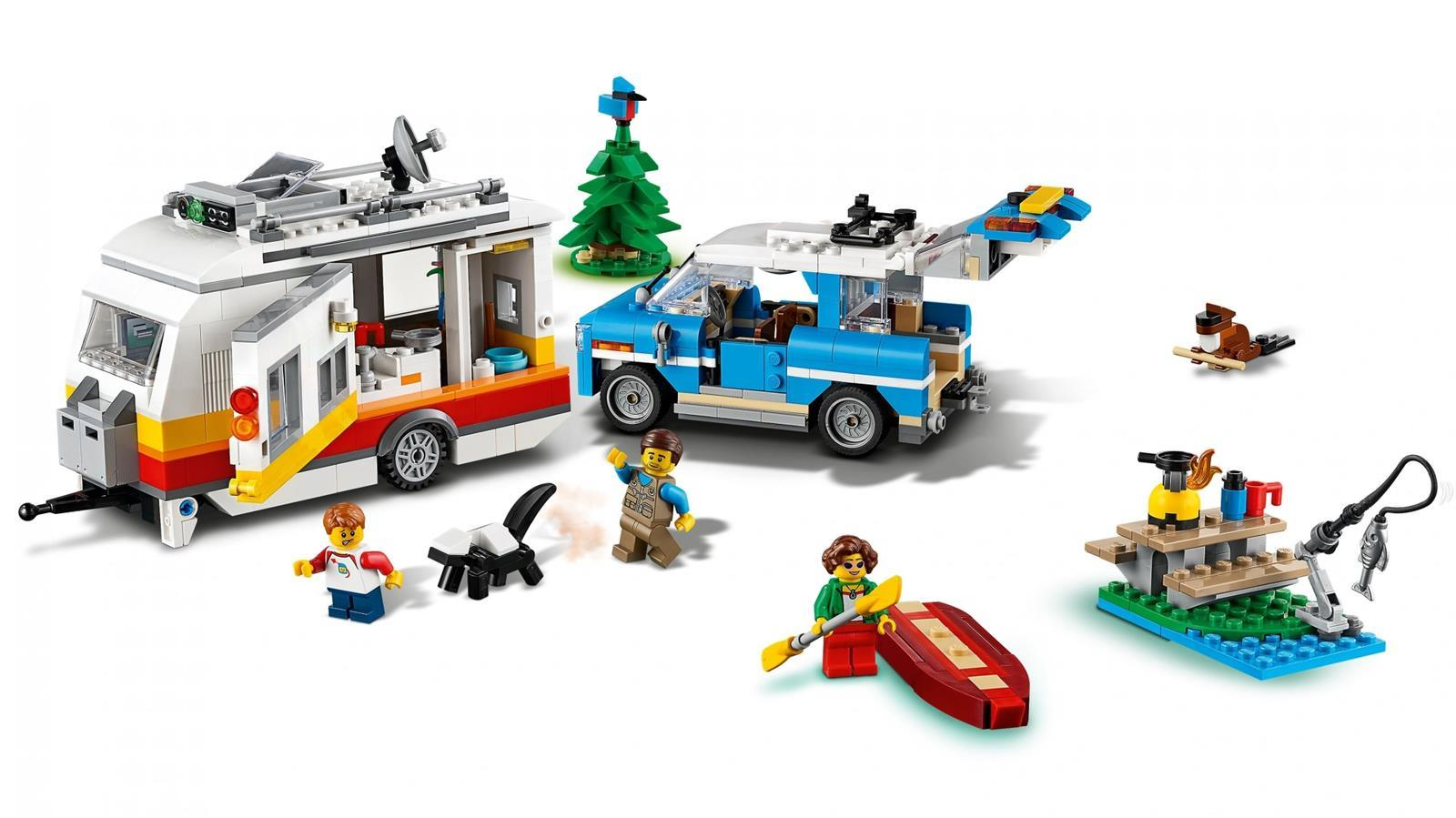 Lego-Urlaubszene mit Wohnwagen, blauem Auto, Minifiguren, Hund, Kajak und Baum auf weißem Hintergrund.