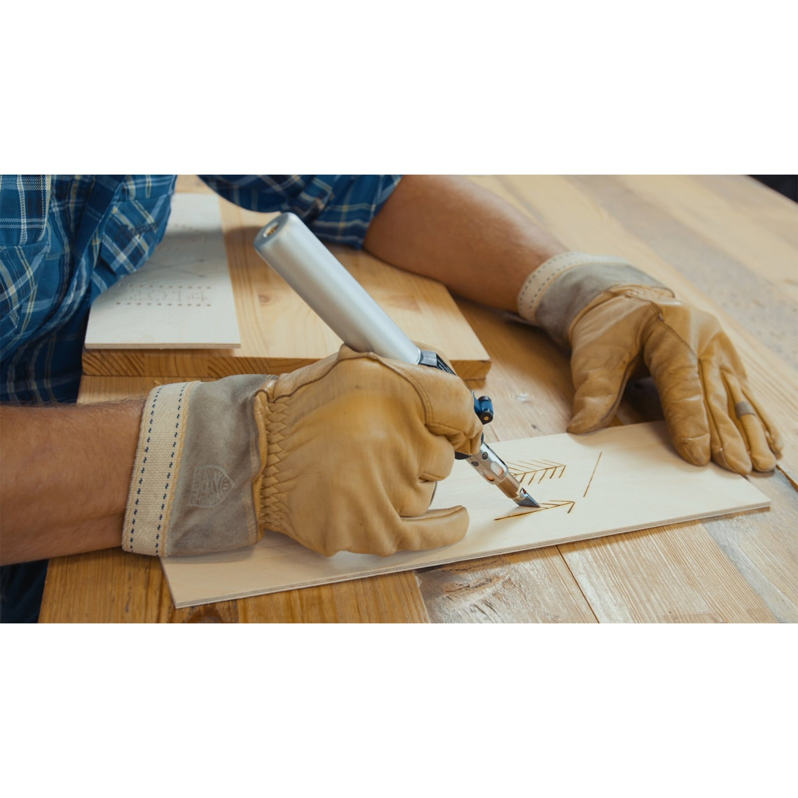 Person mit Arbeitshandschuhen brennt mit einem Pyrografie-Stift ein Muster auf ein dünnes Holzstück.