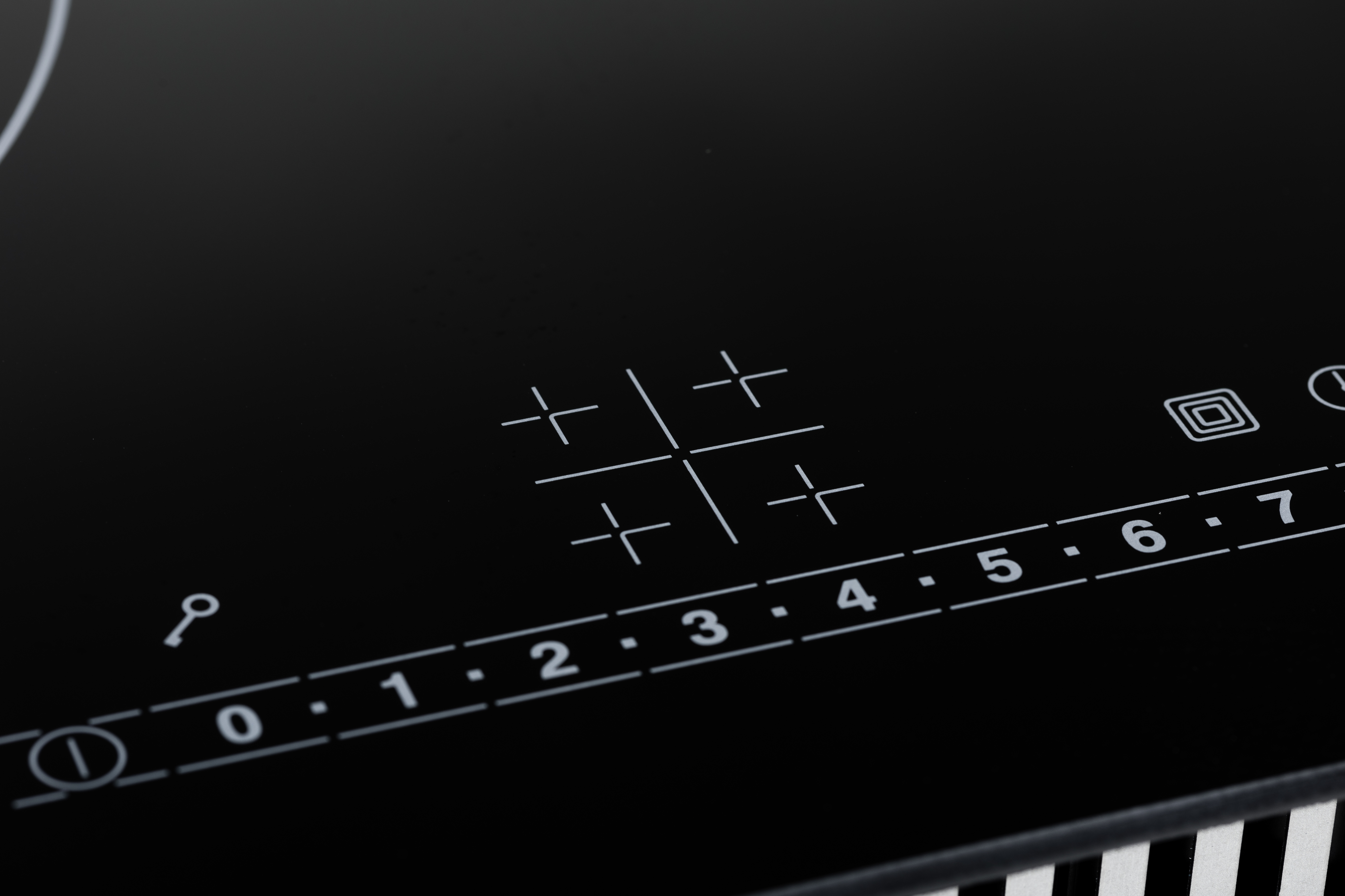 Piano cottura a induzione nero con controlli touch bianchi e numeri da zero a sette.