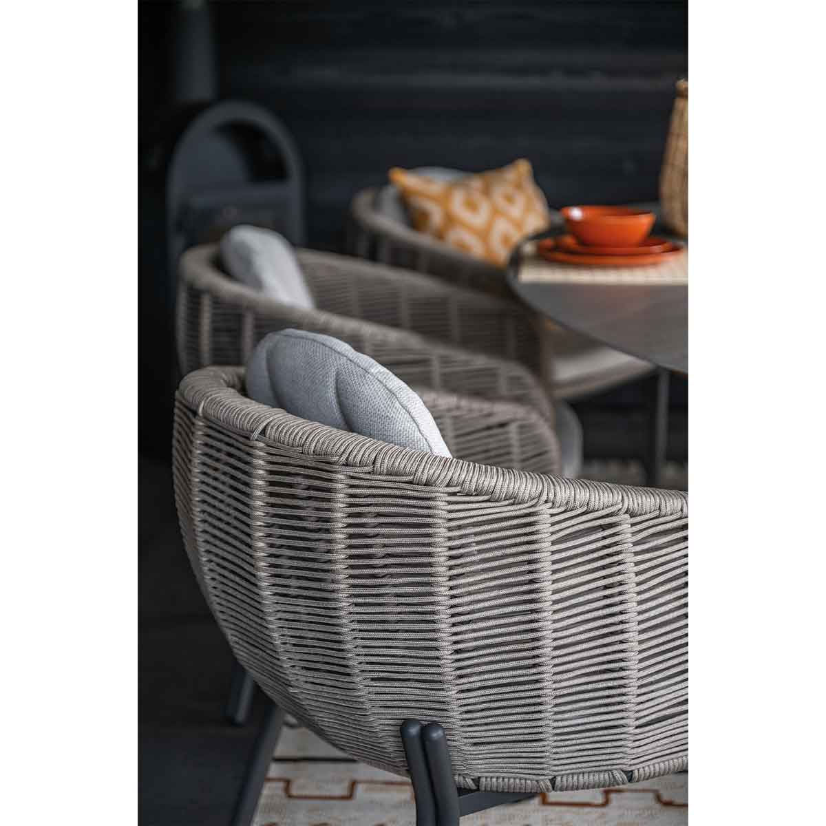 Woven brown wicker armchairs with grey cushions at an outdoor table.