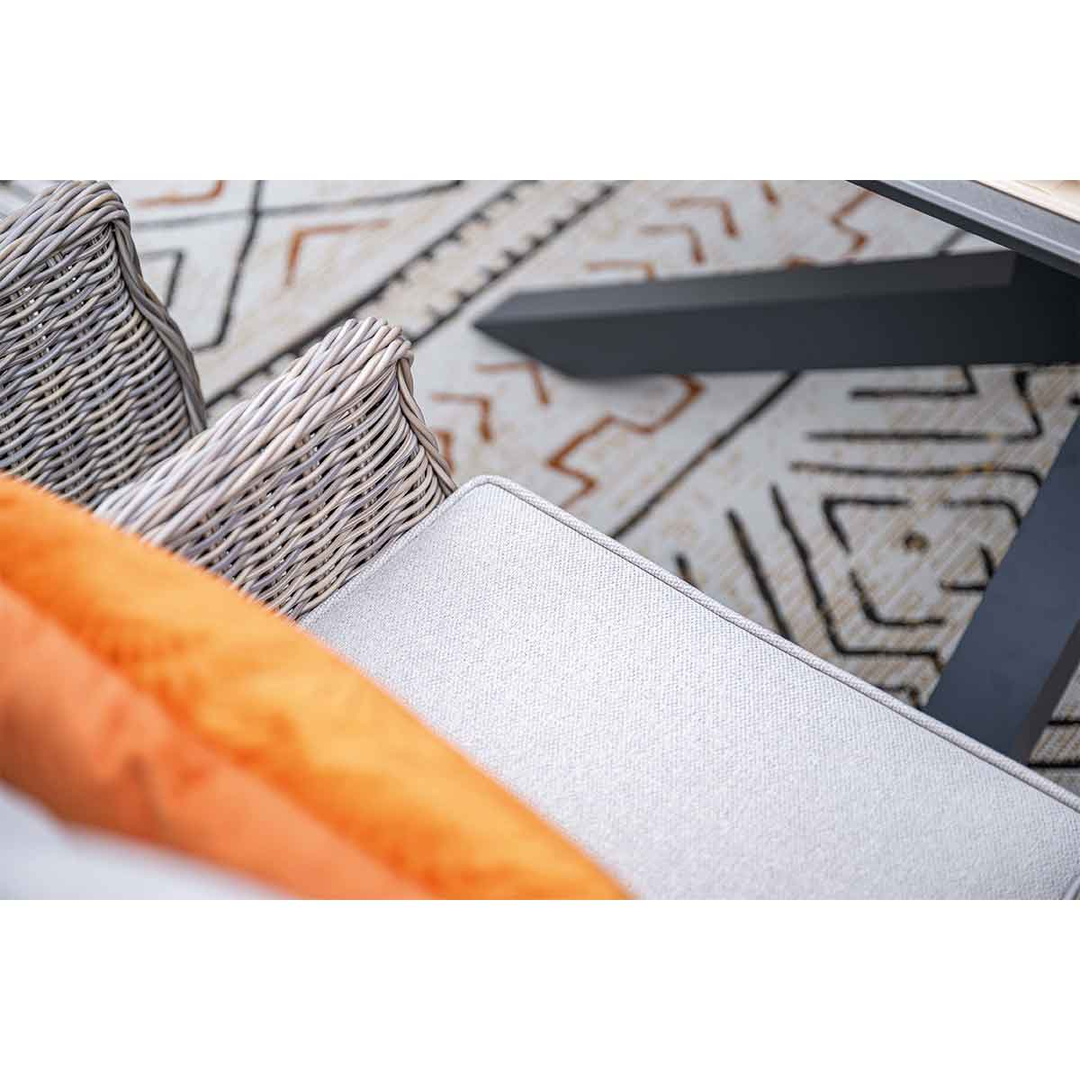 Close-up of wicker armchairs with grey cushions and an orange pillow, set on a patterned rug.