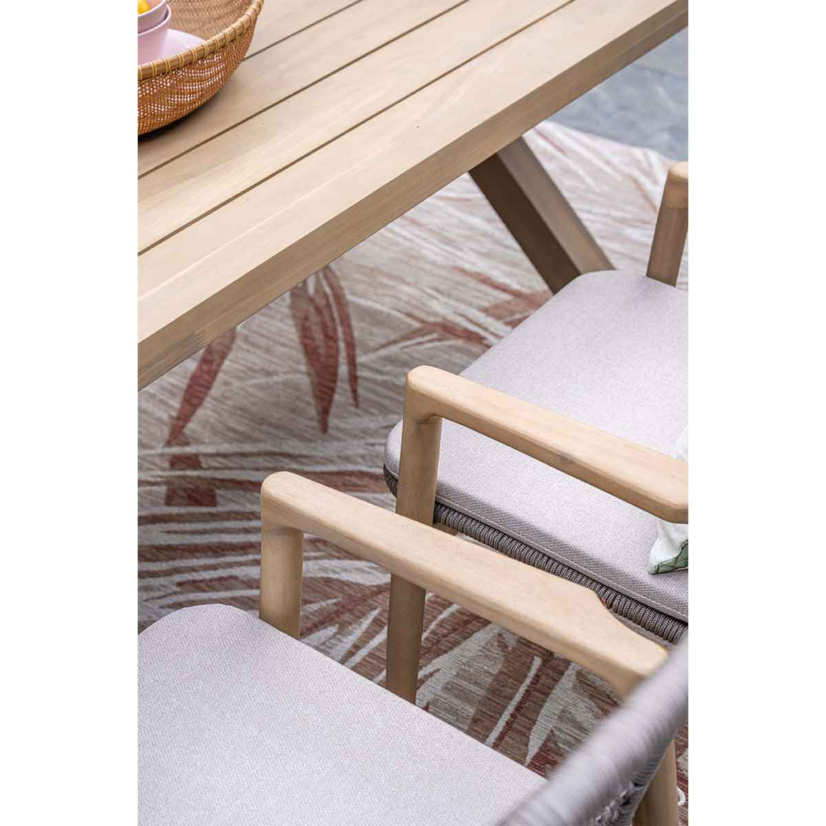 Wooden table and chairs with light cushions on patterned rug.