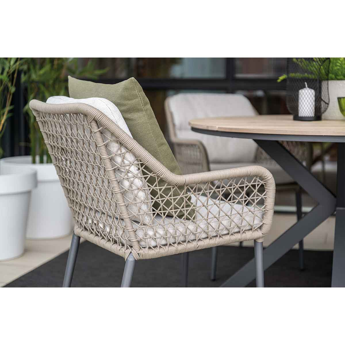 Woven outdoor armchair with white seat pad and green accent pillow at a patio dining table.