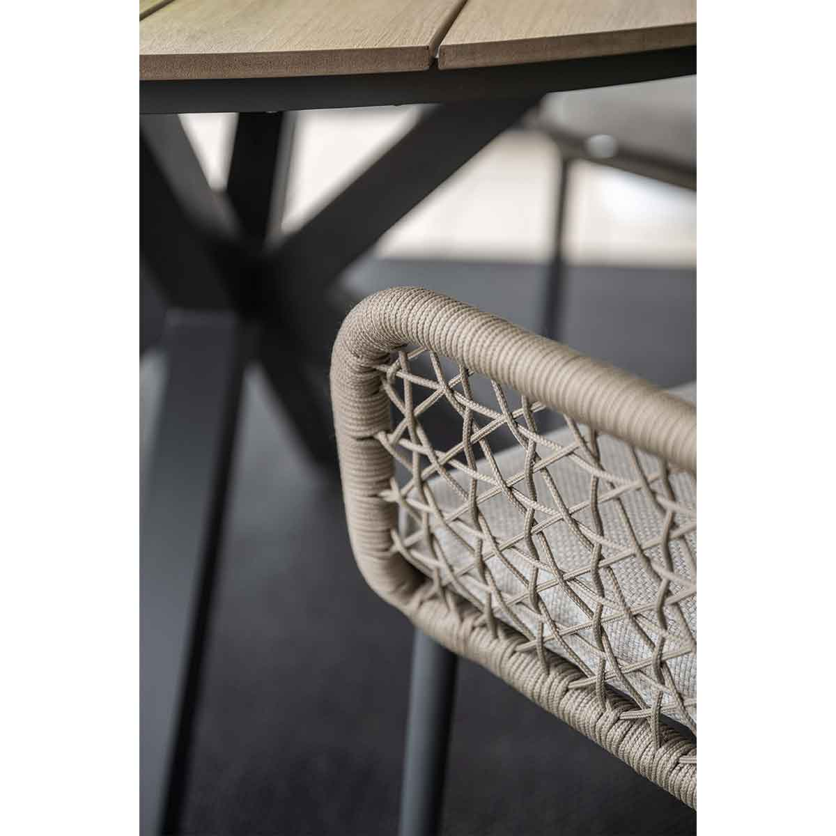 Close-up of a modern chair with beige woven backrest and cushion, with a dark table in the background.