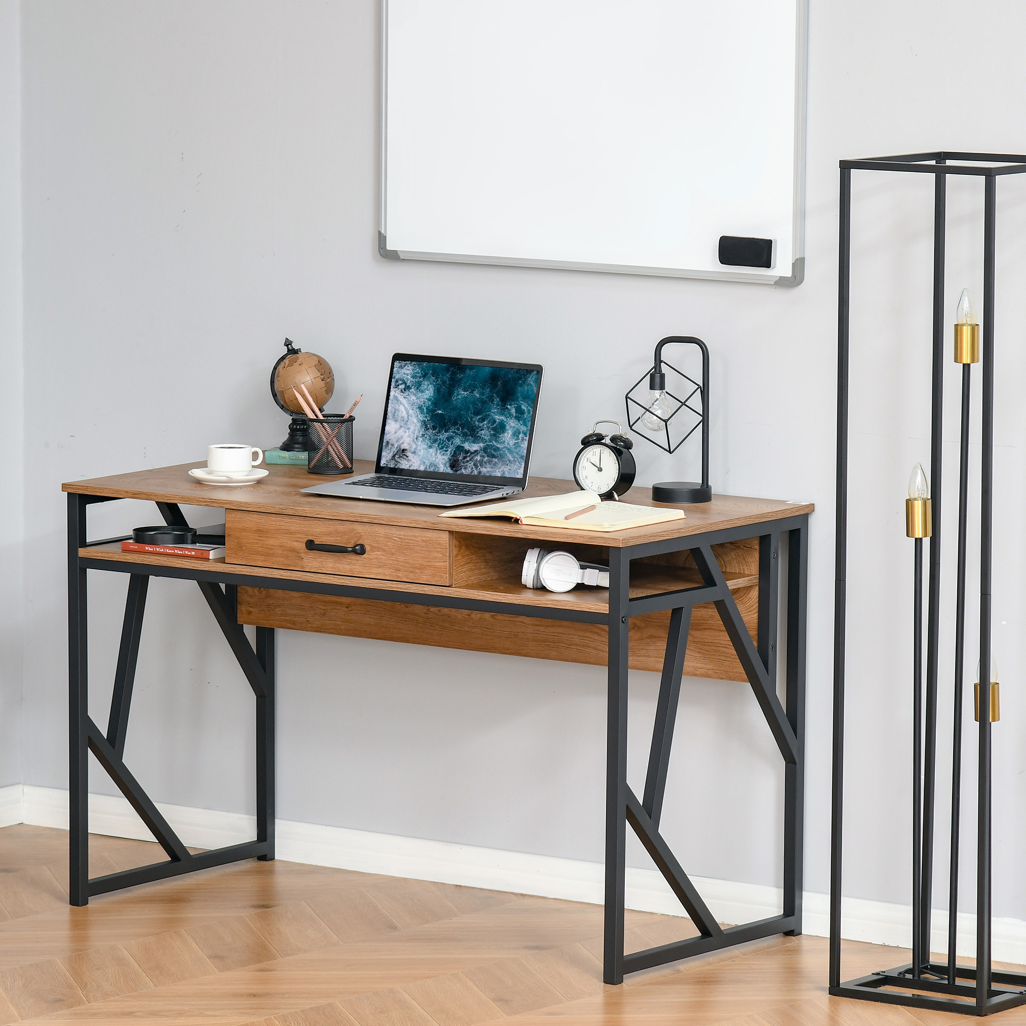 Una scrivania in legno e metallo nero con laptop, mappamondo, lampada e accessori su parete grigia con lavagna.