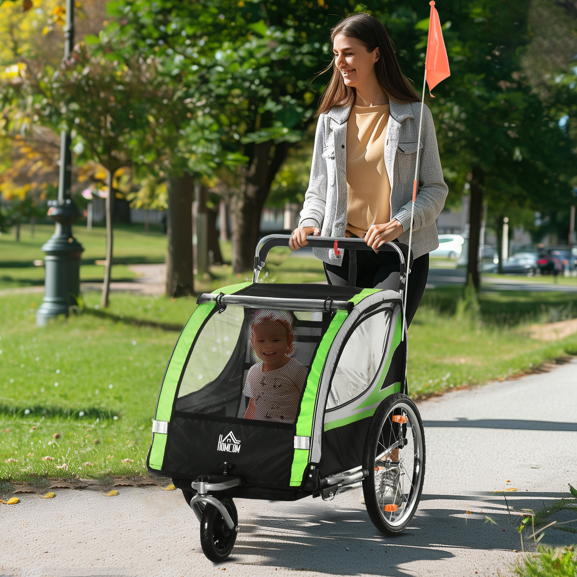 Una donna spinge un passeggino verde e nero con un bambino dentro in un parco.