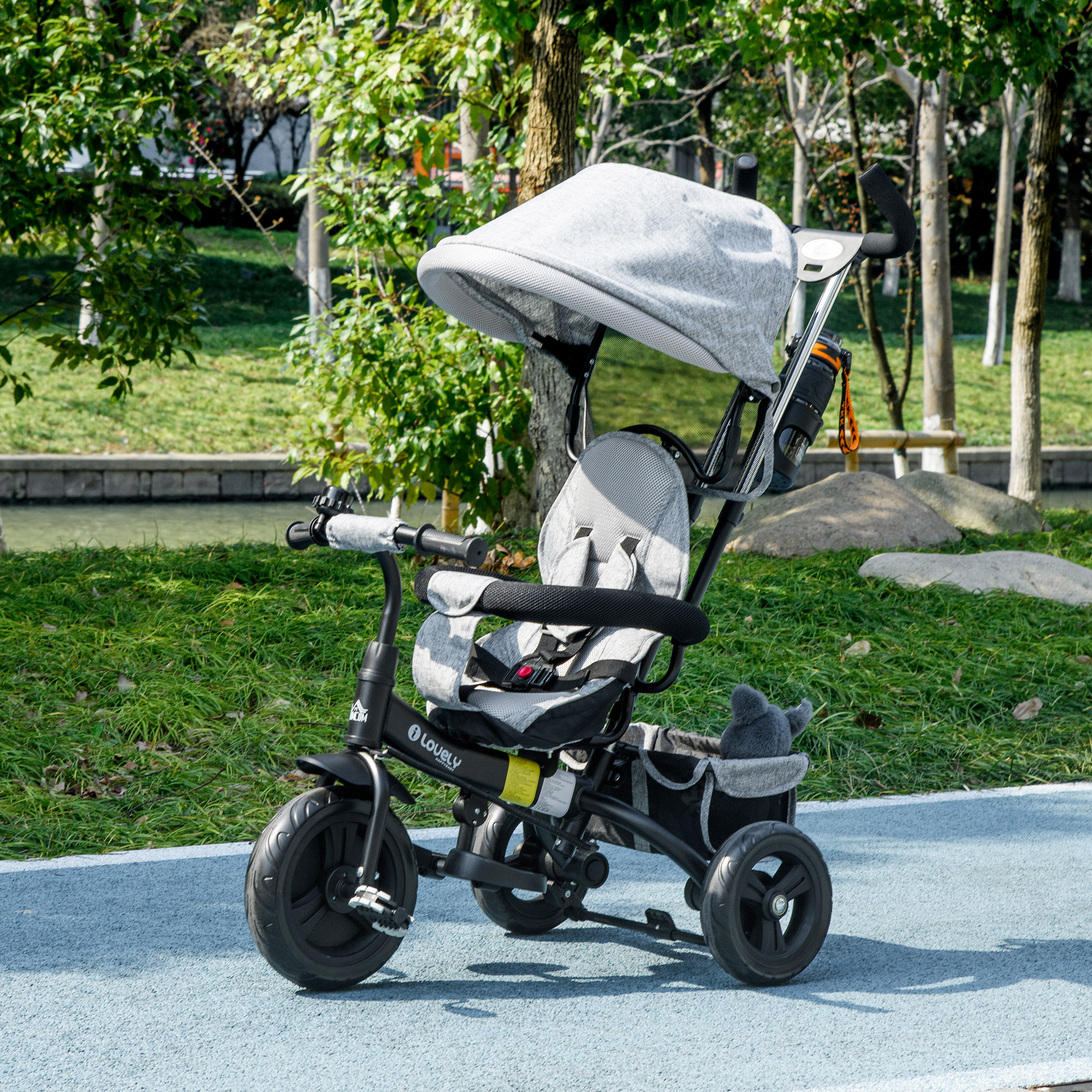 Un triciclo per bambini grigio con capottina si trova su un sentiero asfaltato in un parco.