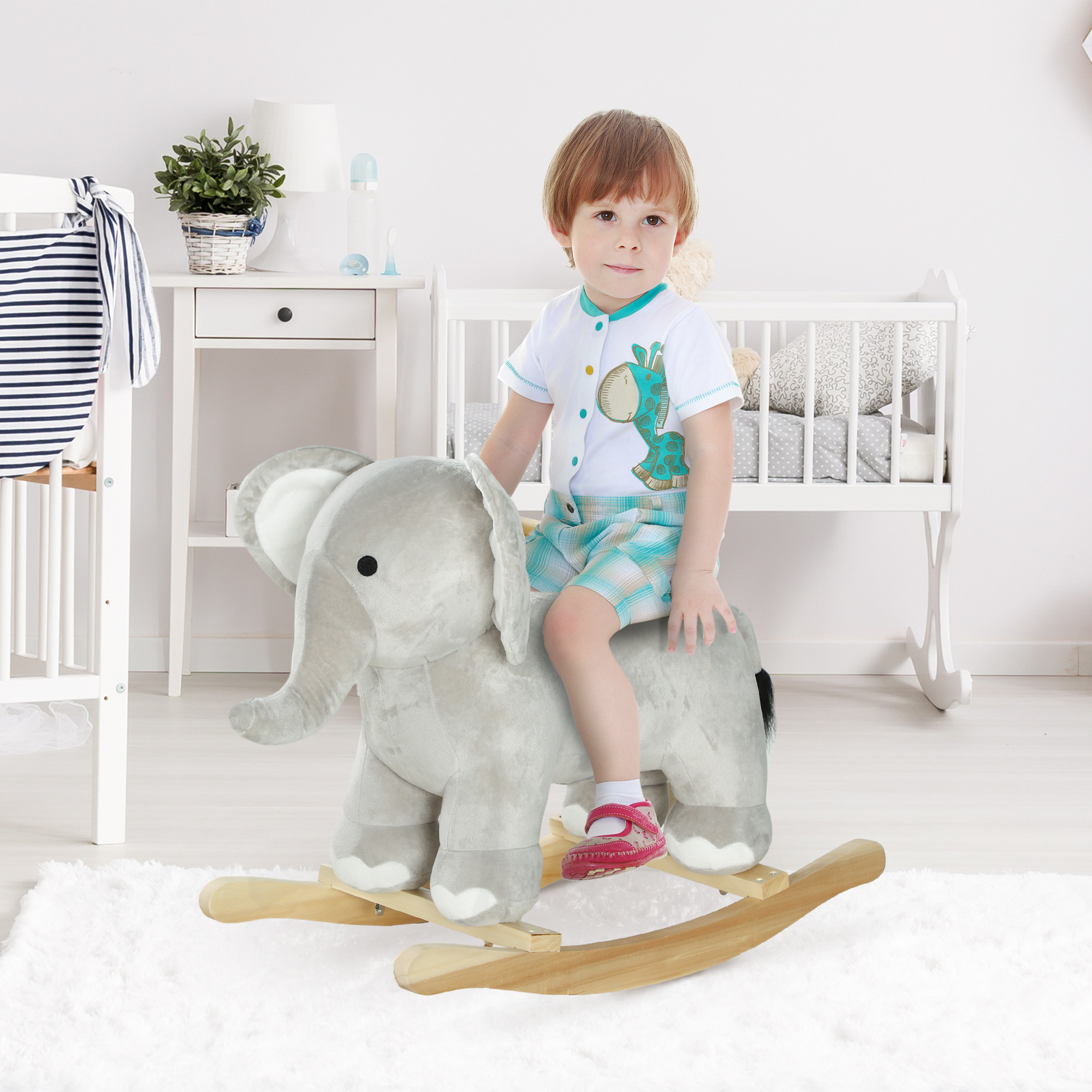 Un bambino cavalca un elefante a dondolo di peluche in una cameretta luminosa con mobili bianchi.