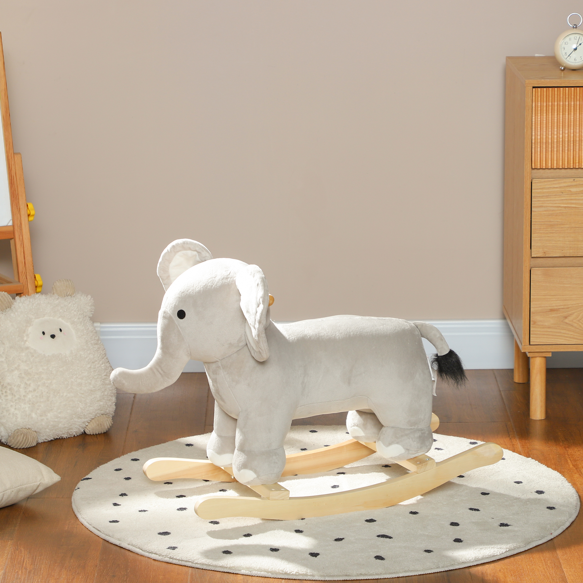 Un elefante giocattolo a dondolo in peluche grigio si trova su un tappeto a pois bianchi e neri.