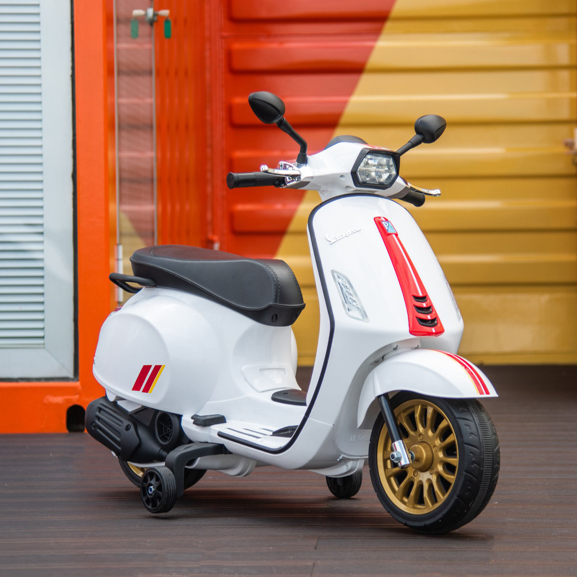 Uno scooter per bambini bianco con rotelle di supporto davanti a una parete rossa e gialla.