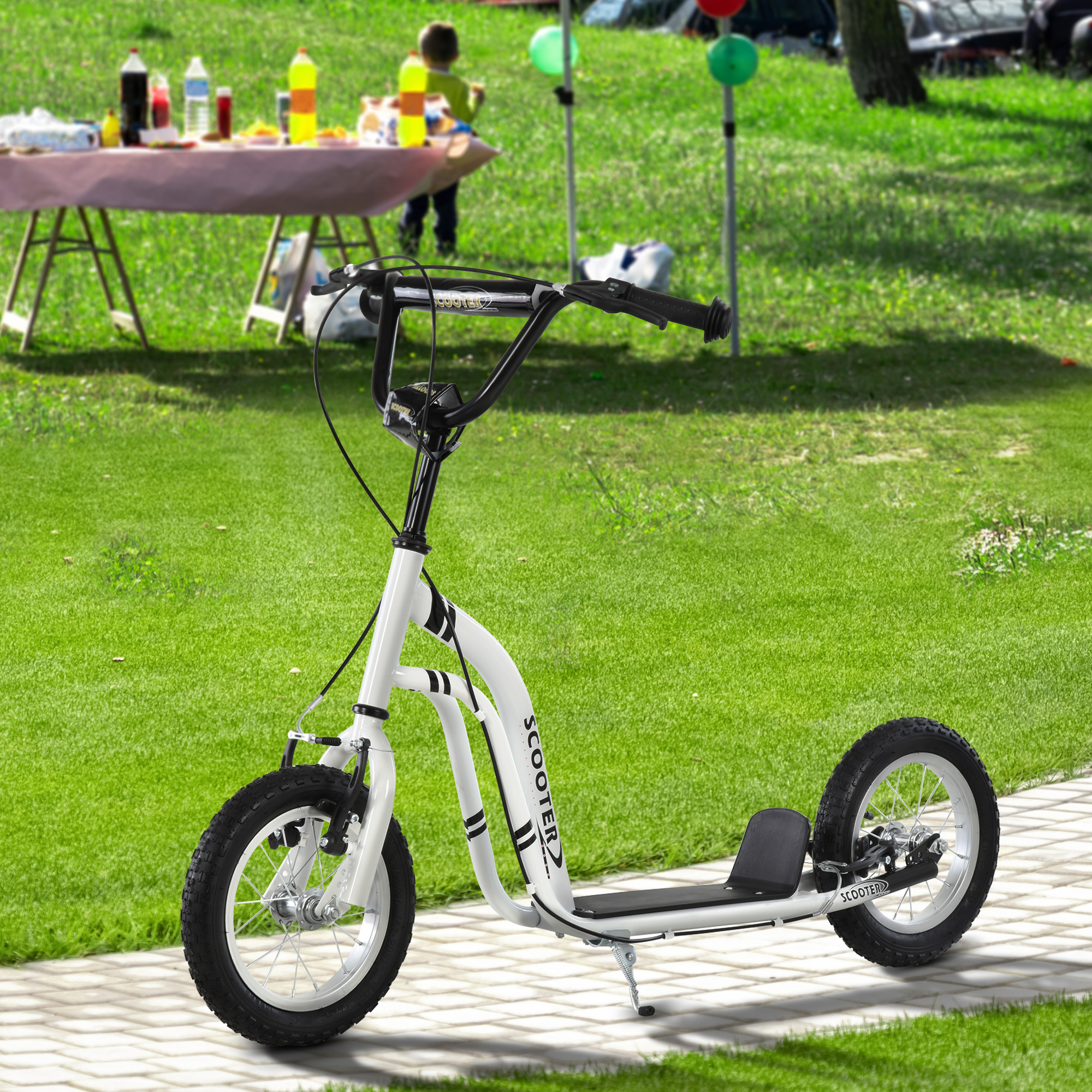 Un monopattino per bambini bianco su un sentiero del parco, con tavolo da picnic e prato sullo sfondo.