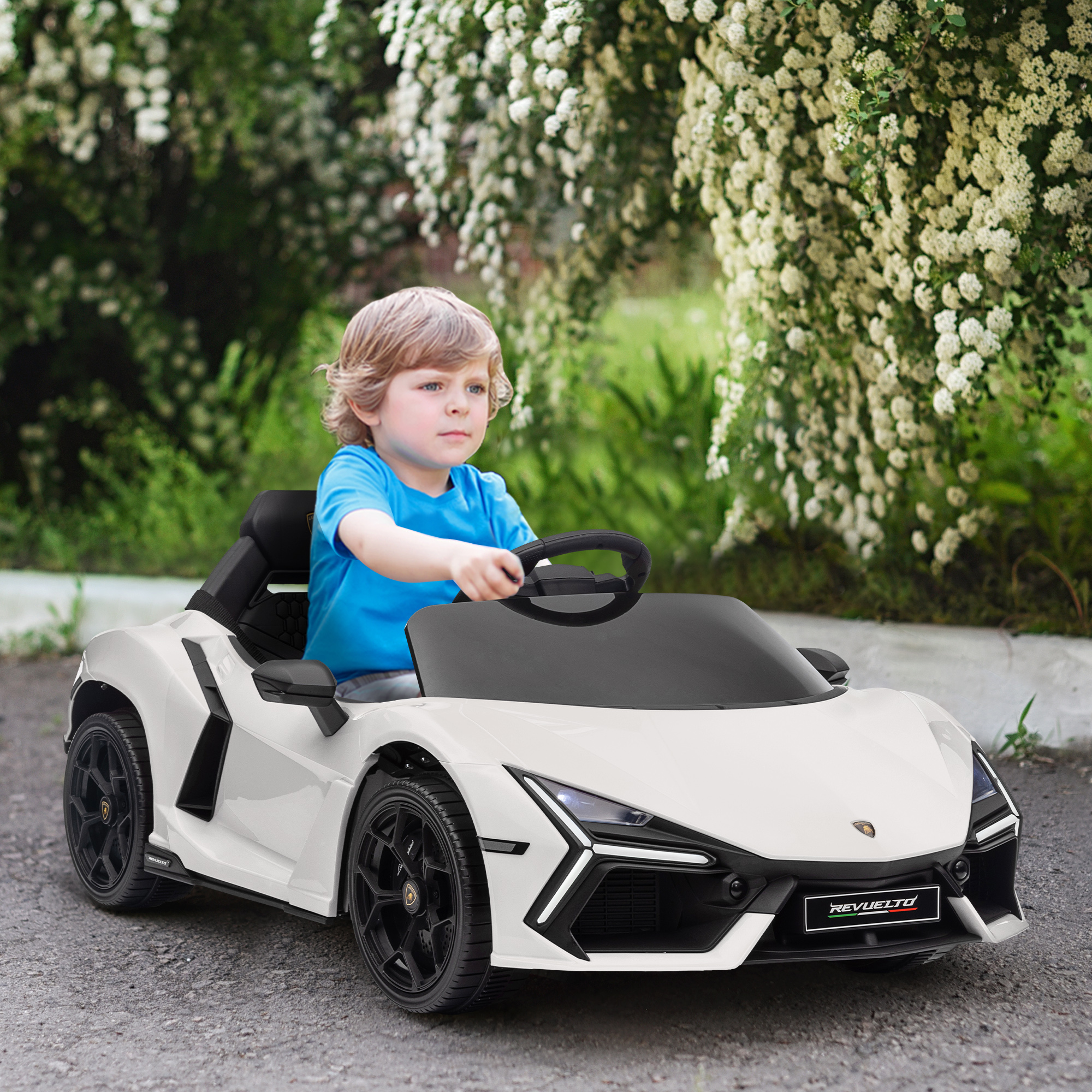 Un bambino con la maglietta blu guida una macchinina sportiva bianca su una strada con cespugli.