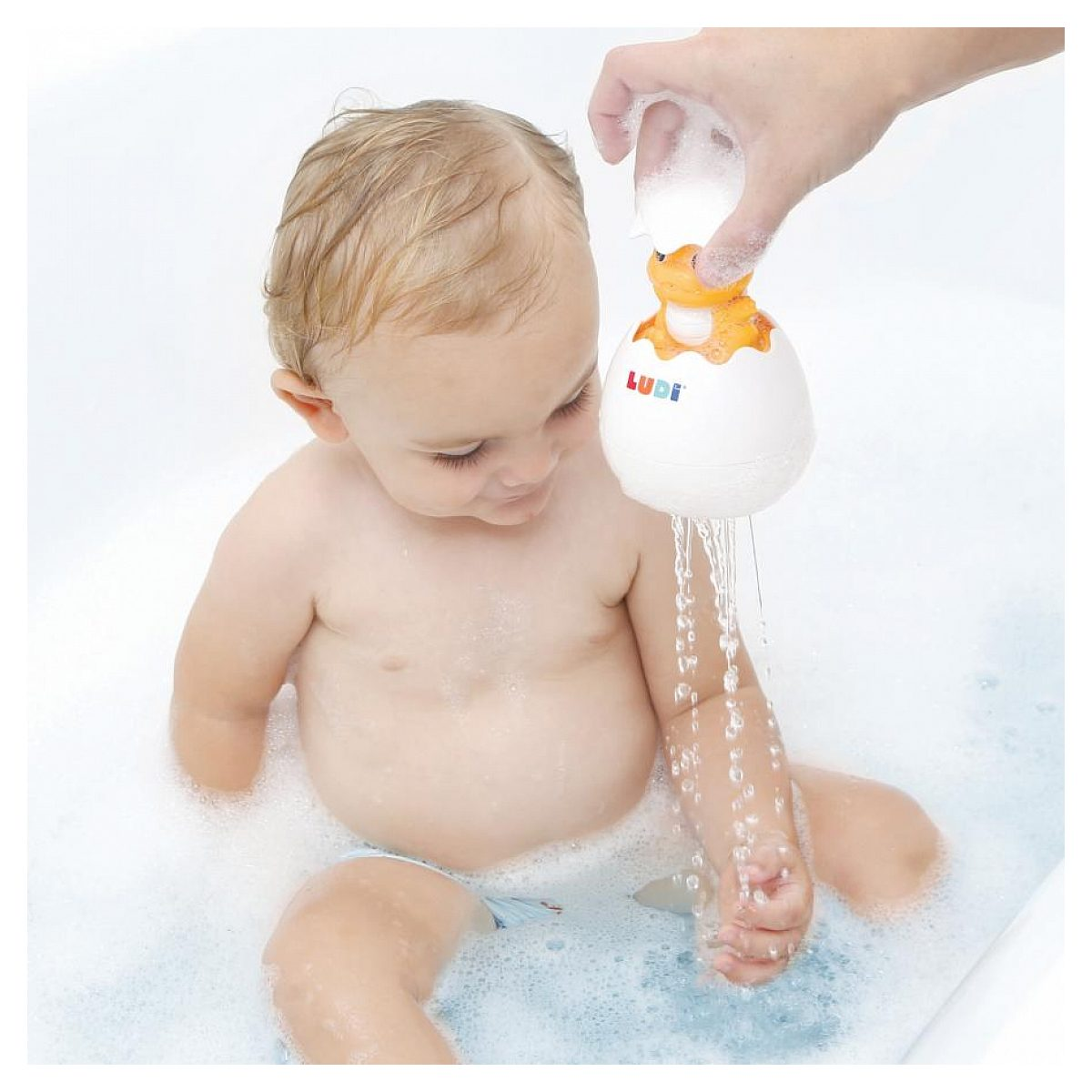 Ein Baby sitzt in einer Badewanne, während Wasser aus einem spielzeugartigen Ei über seine Hand läuft.