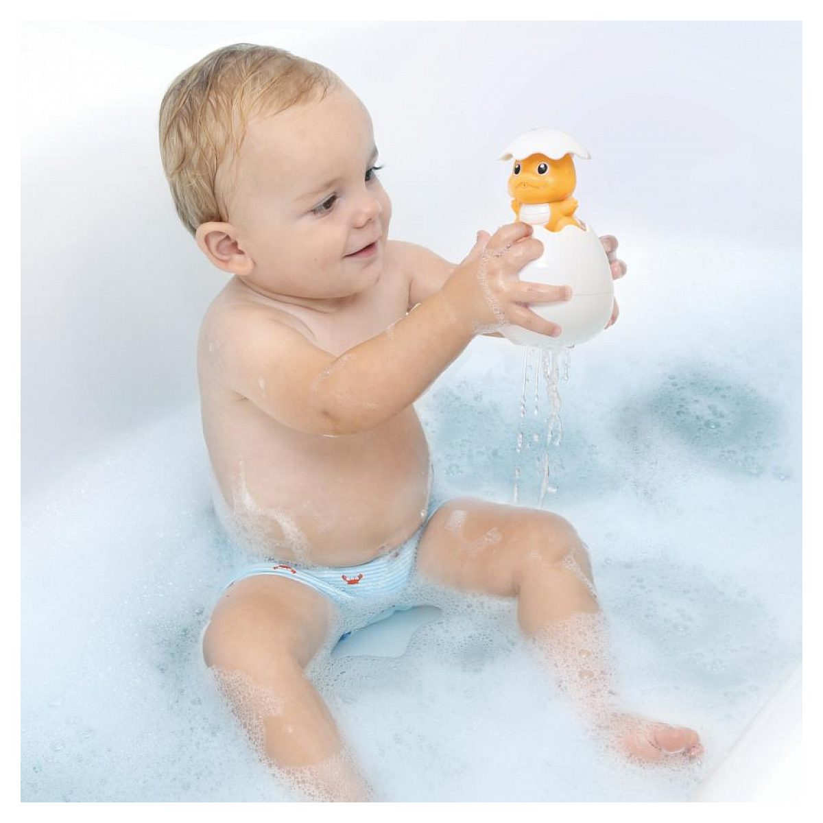 Kleinkind sitzt in einer Badewanne mit Schaum und hält ein Spielzeug mit einer kleinen gelben Figur.